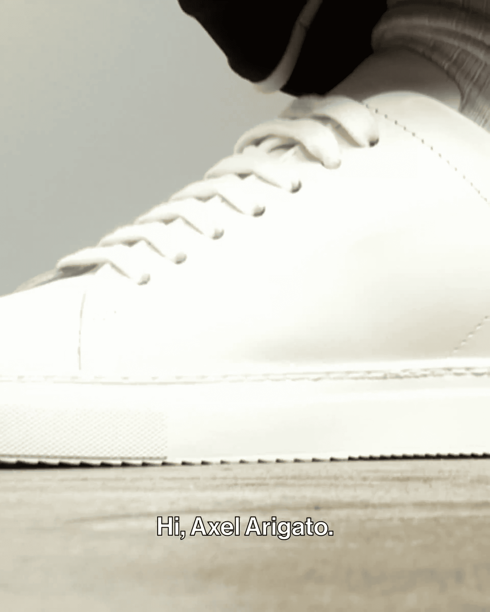 Close-up of a white sneaker with a thick sole on a wooden surface. Text at the bottom reads, "Hi, Axel Arigato."