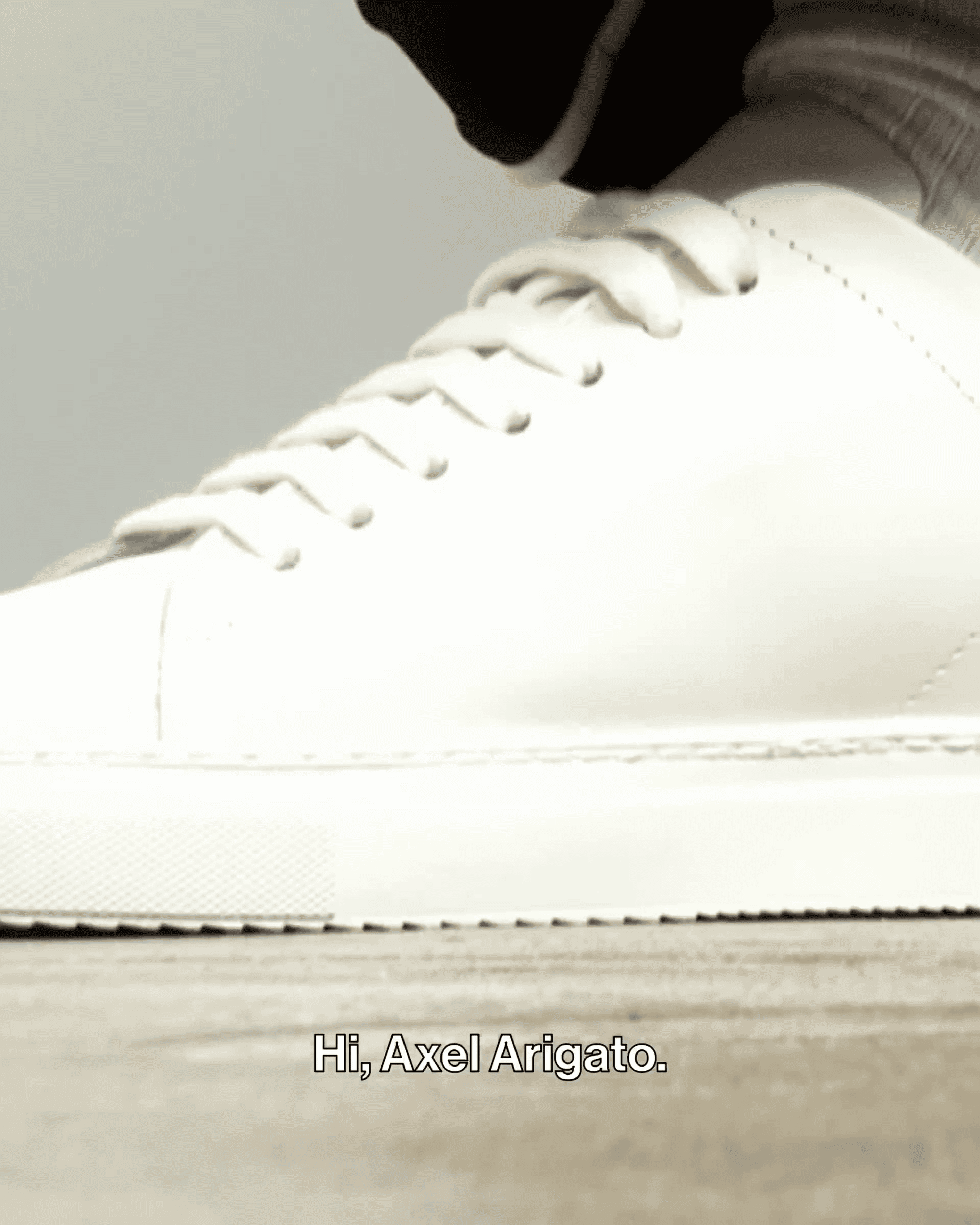 Close-up of a white sneaker with a thick sole on a wooden surface. Text at the bottom reads, "Hi, Axel Arigato."