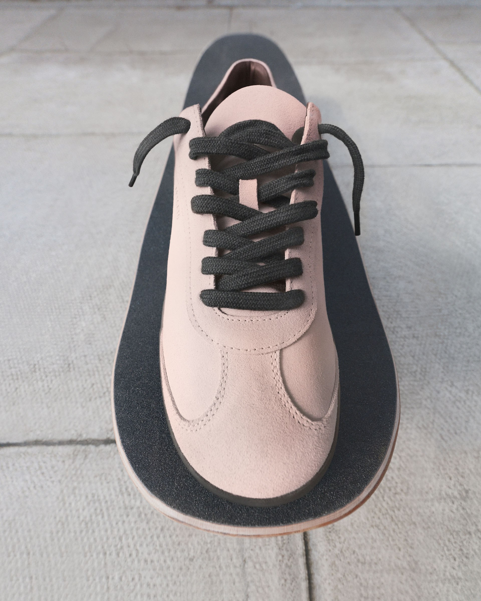 A beige sneaker with black laces rests on a skateboard with a textured black surface, placed on a concrete floor.