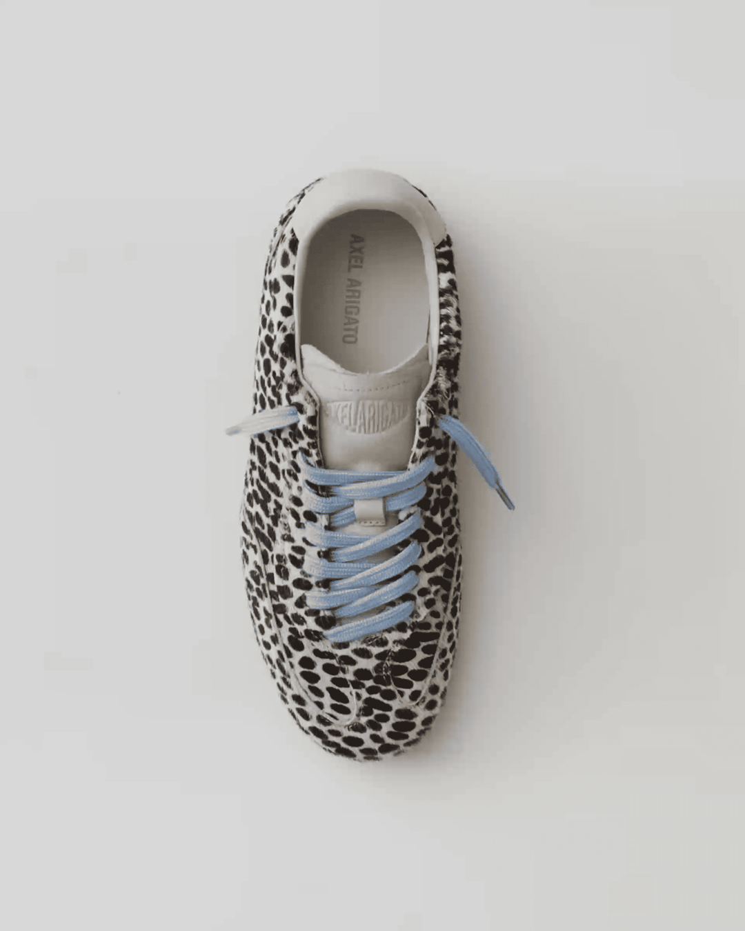 Black and white spotted sneaker with light blue laces, viewed from above against a plain background.