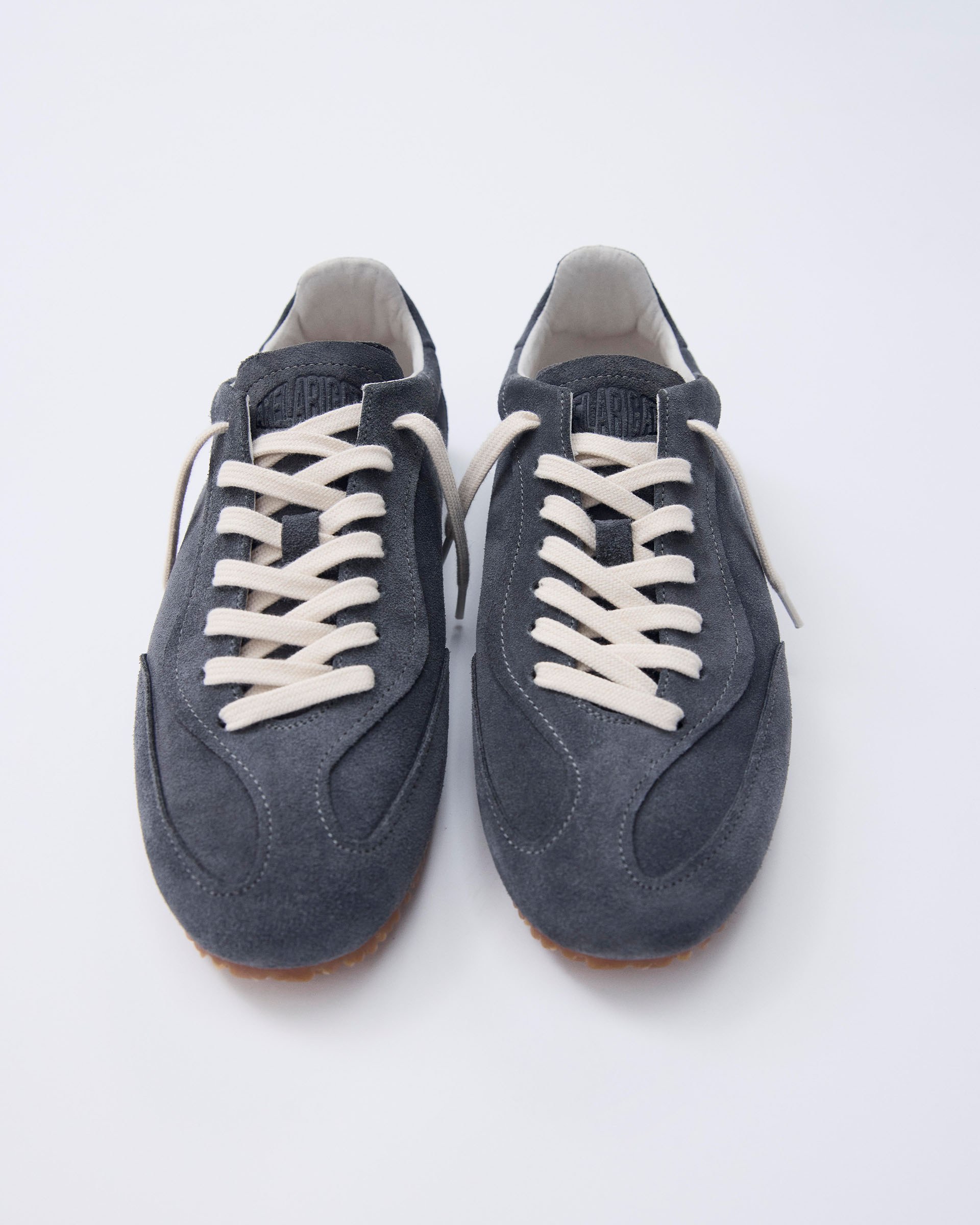 Gray suede sneakers with white laces and brown soles, viewed from above on a white background.