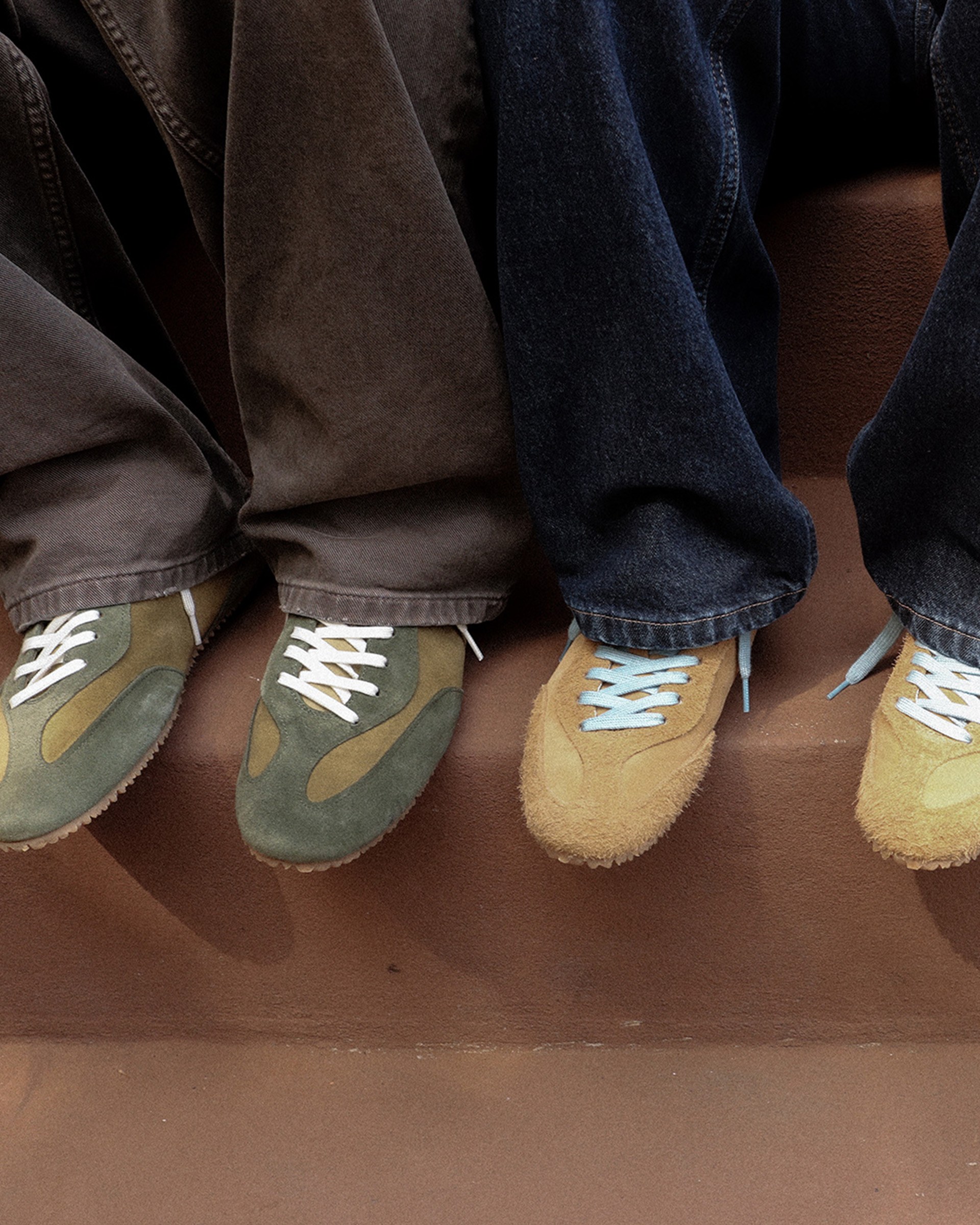 Three people sitting on steps, wearing wide-leg jeans and colorful sneakers; one pair of green and two pairs of tan with white laces.