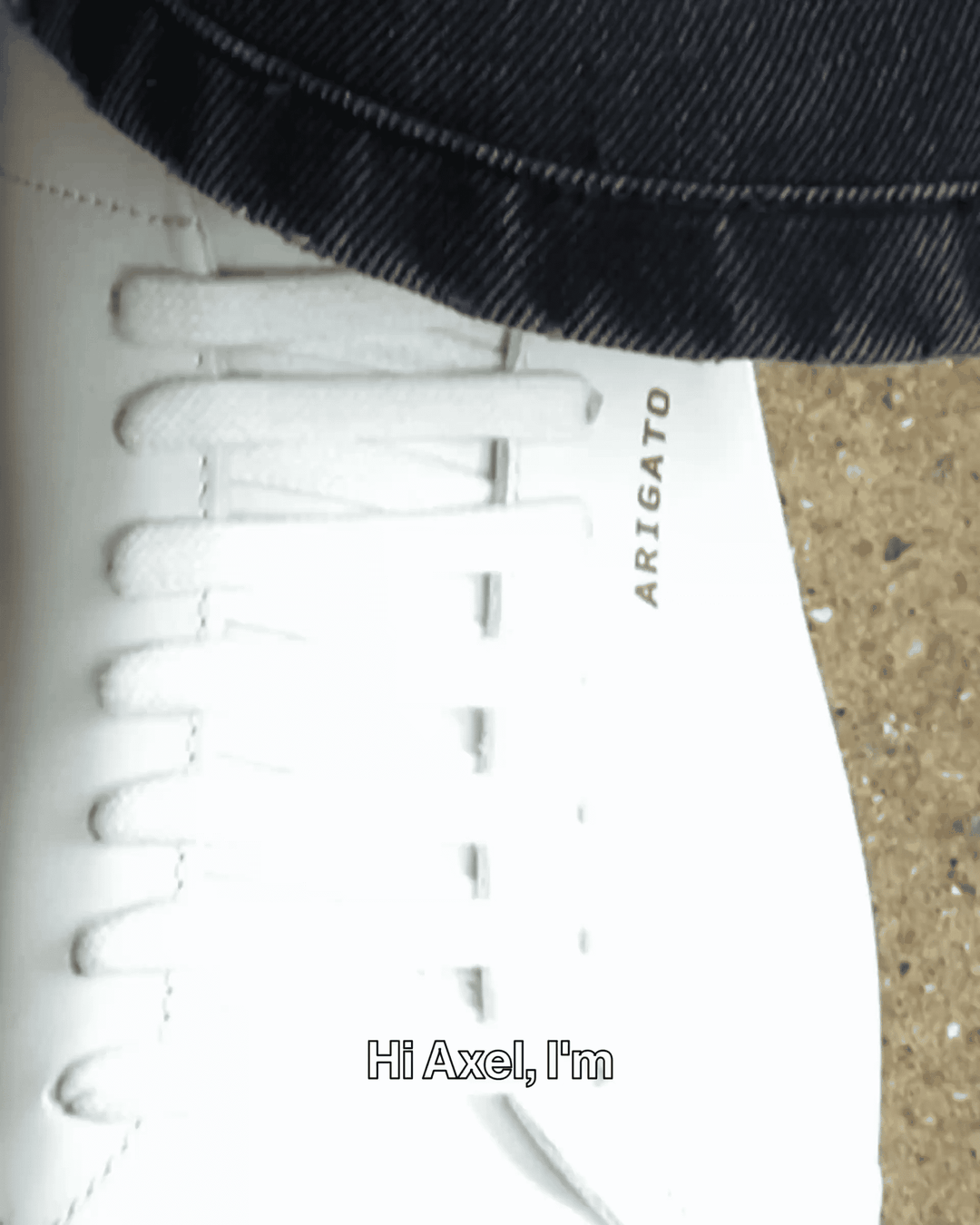 A close-up of a white sneaker with "ARIGATO" written on it, worn with dark jeans. The text overlay says, "Hi Axel, I'm."