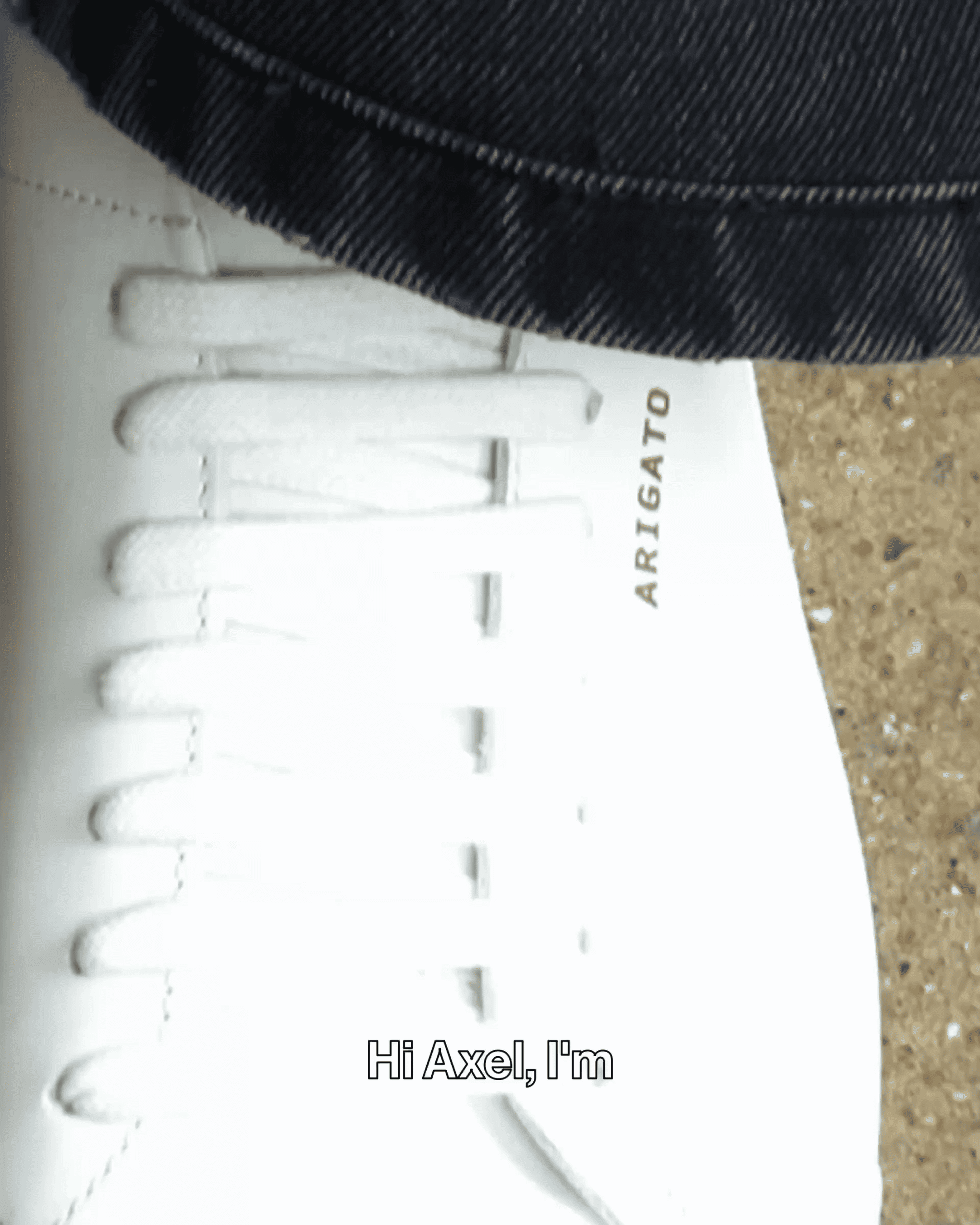 A close-up of a white sneaker with "ARIGATO" written on it, worn with dark jeans. The text overlay says, "Hi Axel, I'm."