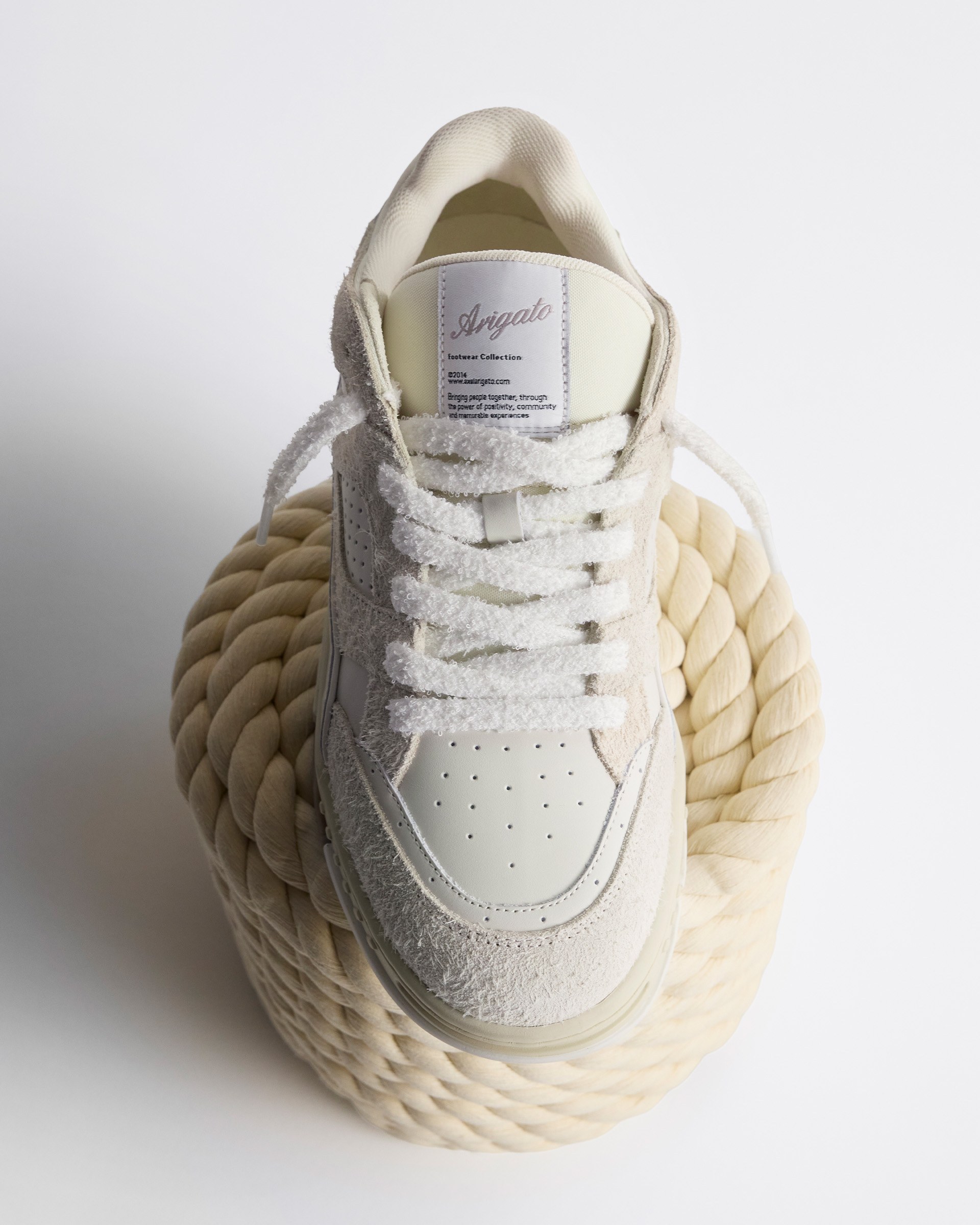 A white and beige sneaker with textured laces rests on a coiled rope, viewed from above against a plain background.