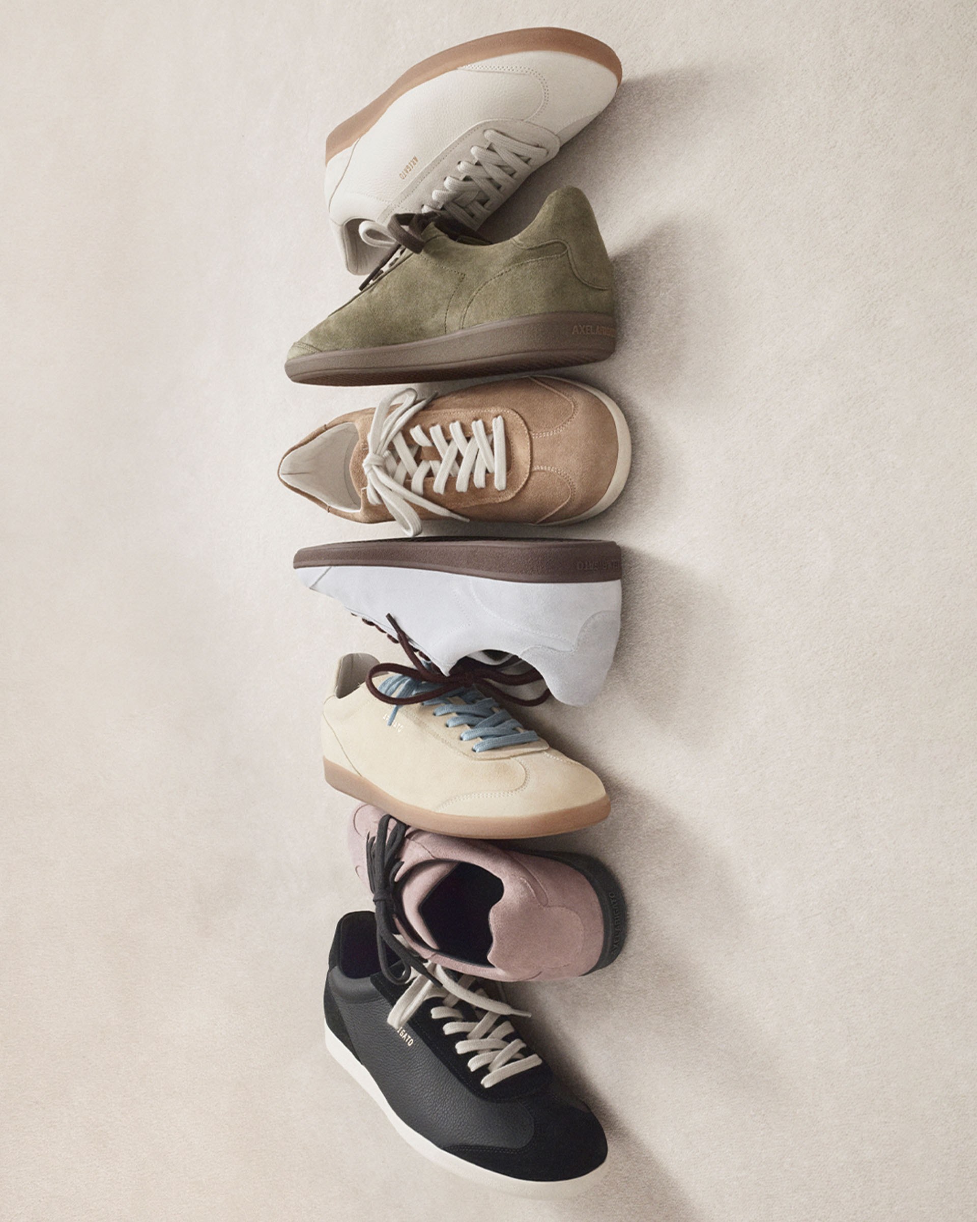 Six sneakers in various colors—white, olive, beige, brown, cream, and black—neatly aligned on a light surface.