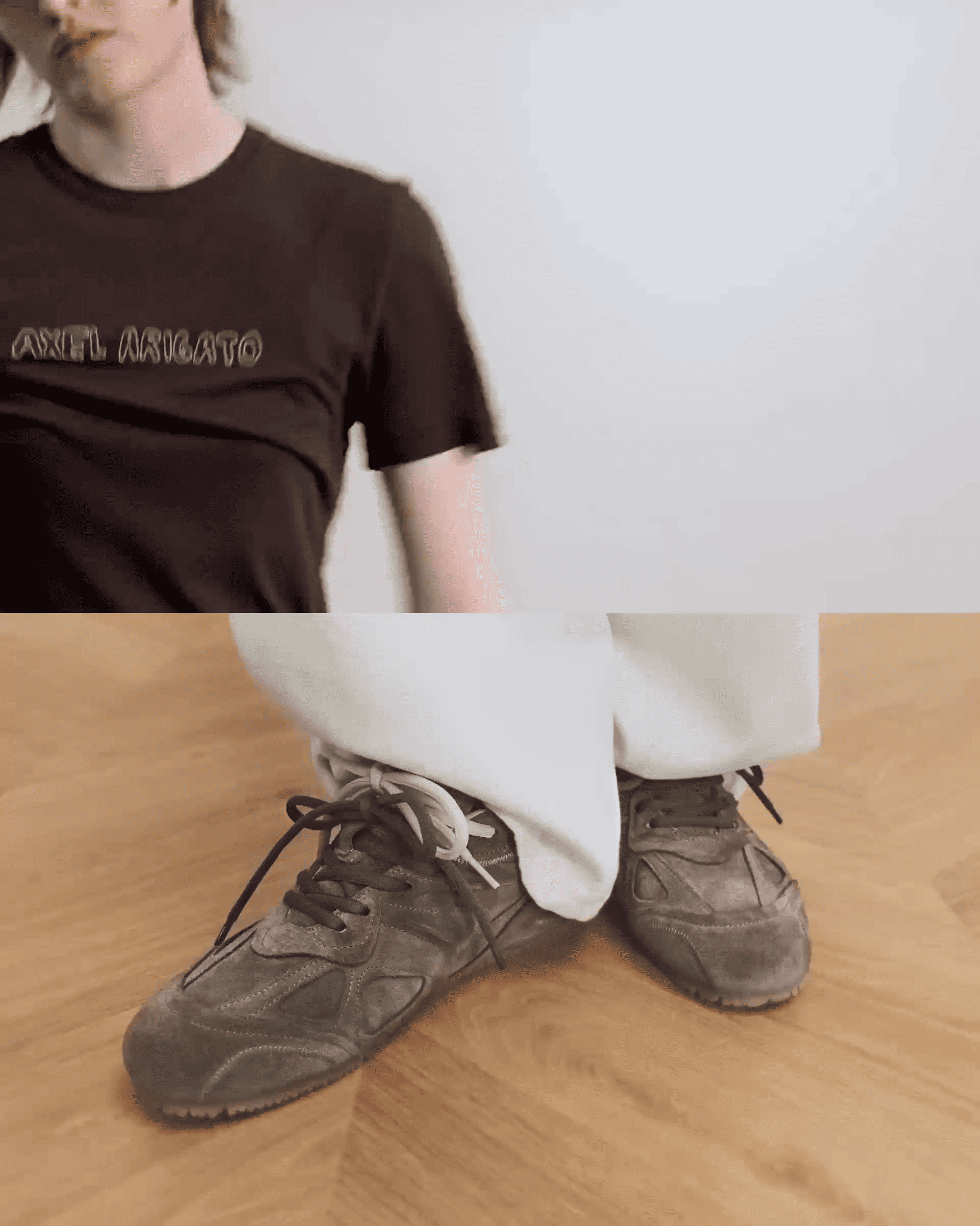 Person in a black Axel Arigato shirt and white pants, with gray sneakers on a wooden floor. Image split effect.