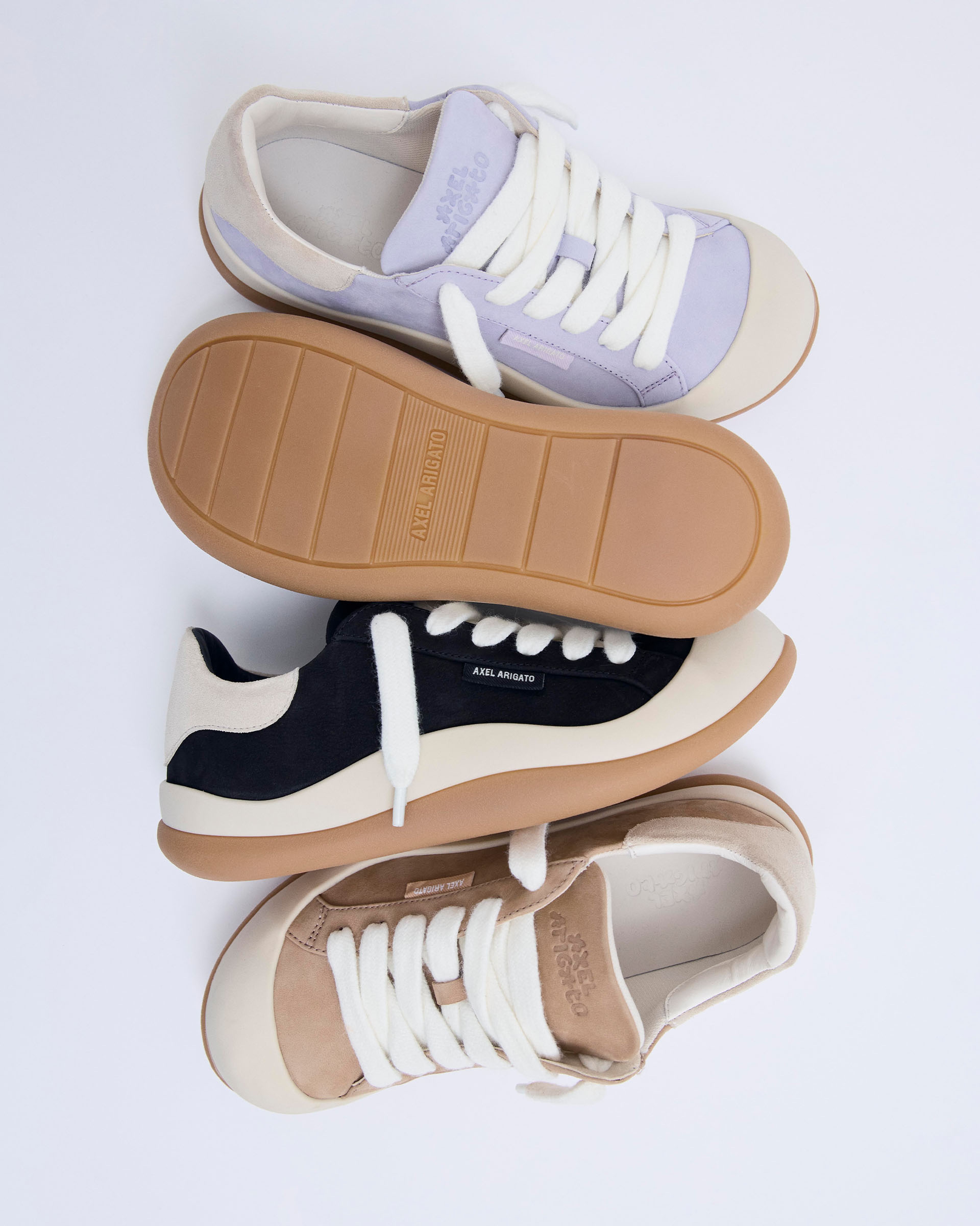 Three pairs of sneakers in purple, black, and beige, arranged creatively; showing laces and gum soles on a white background.