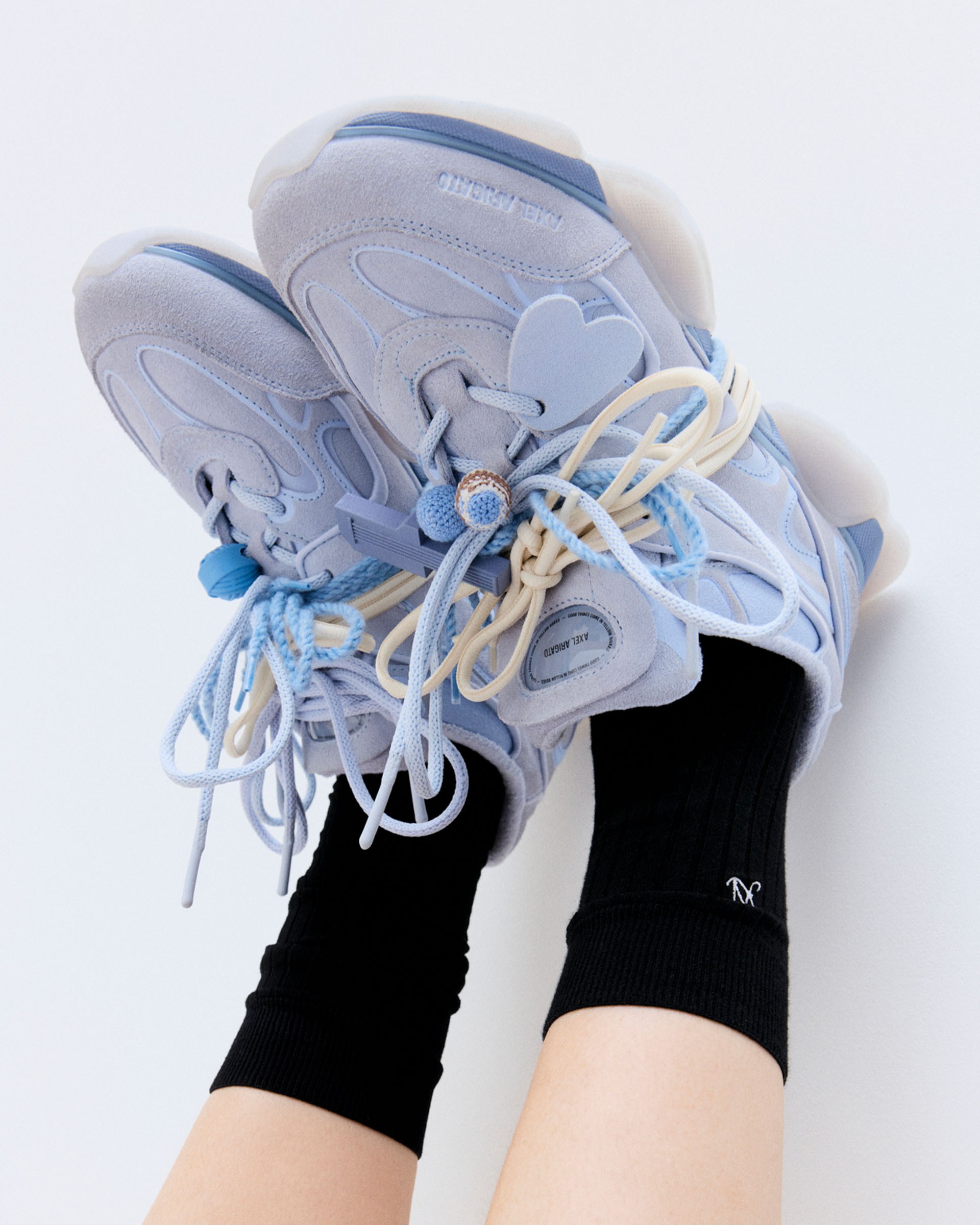 Person wearing light blue sneakers with heart details and black socks against a white background.