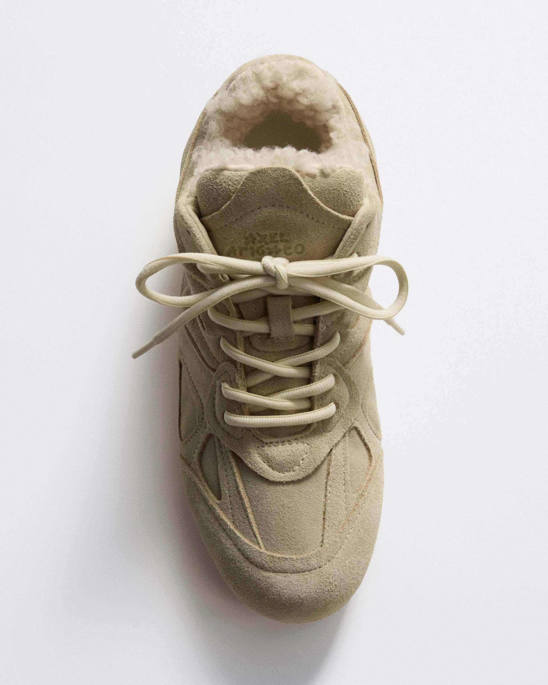 Top view of a beige suede sneaker with a plush interior and beige laces, set against a plain white background.