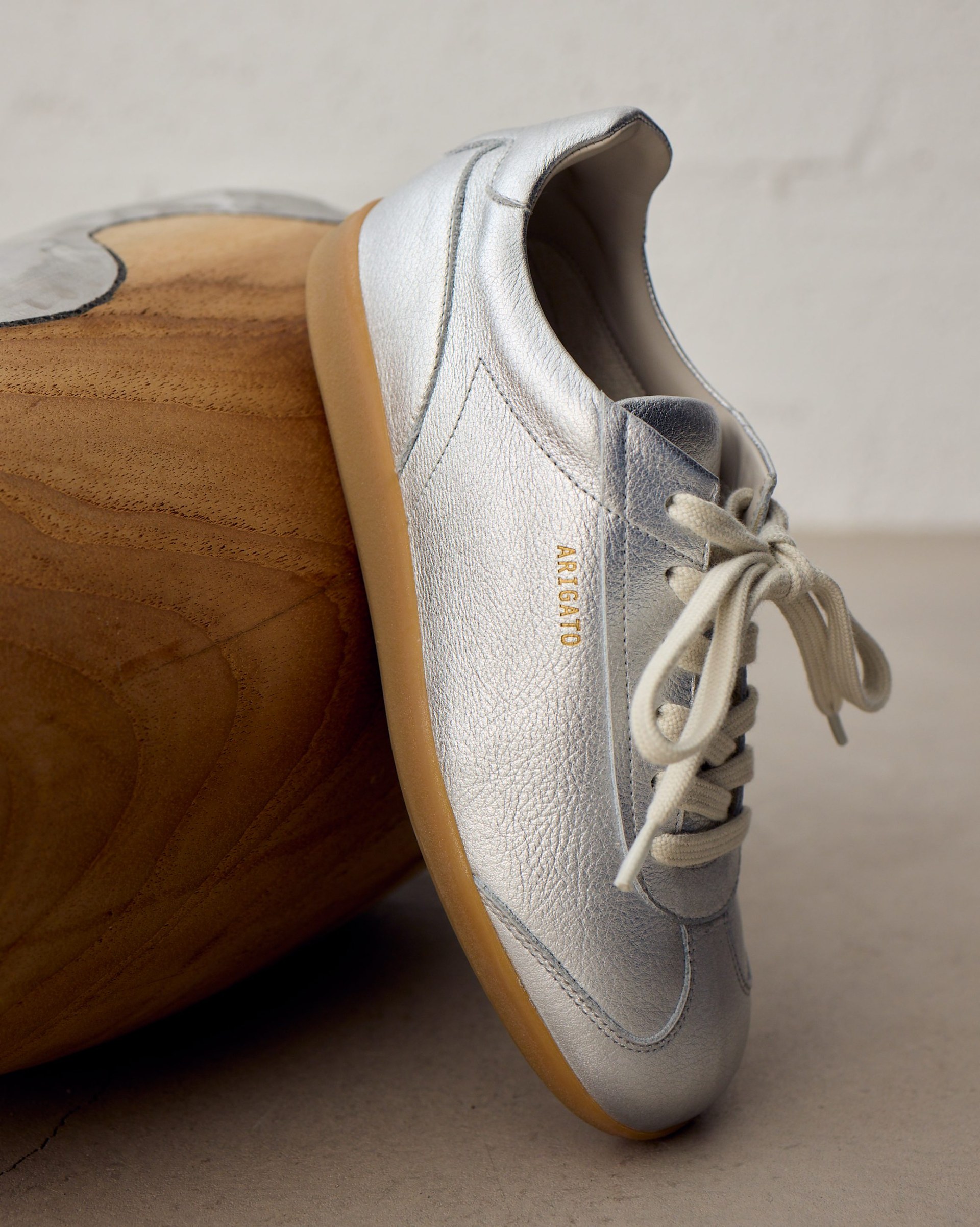 Silver sneaker with cream laces and a gum sole, resting against a wooden surface.
