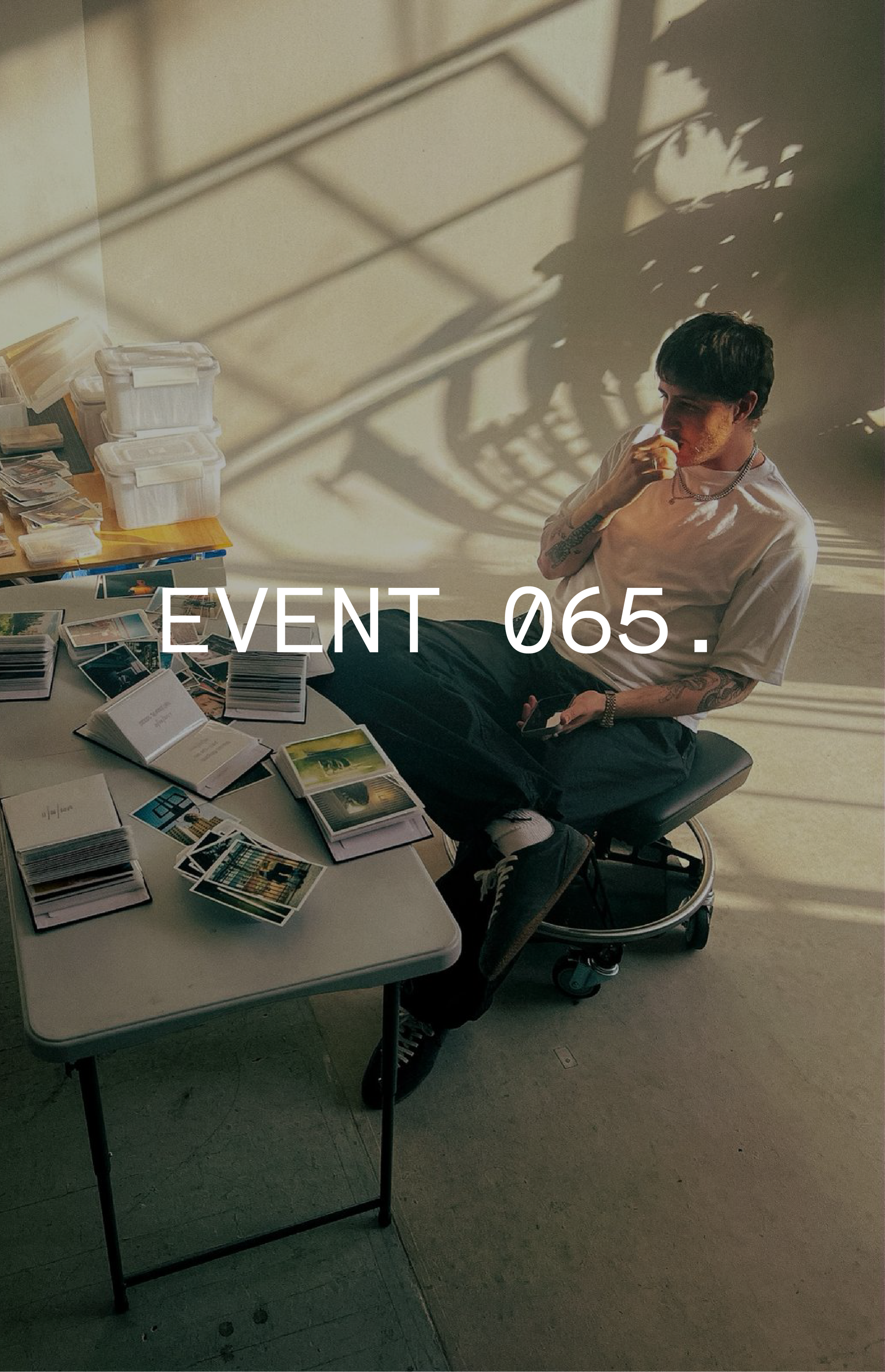 A person sits thoughtfully at a table covered with books and papers, under dappled sunlight, with the words "EVENT 065" overlaid on the image.