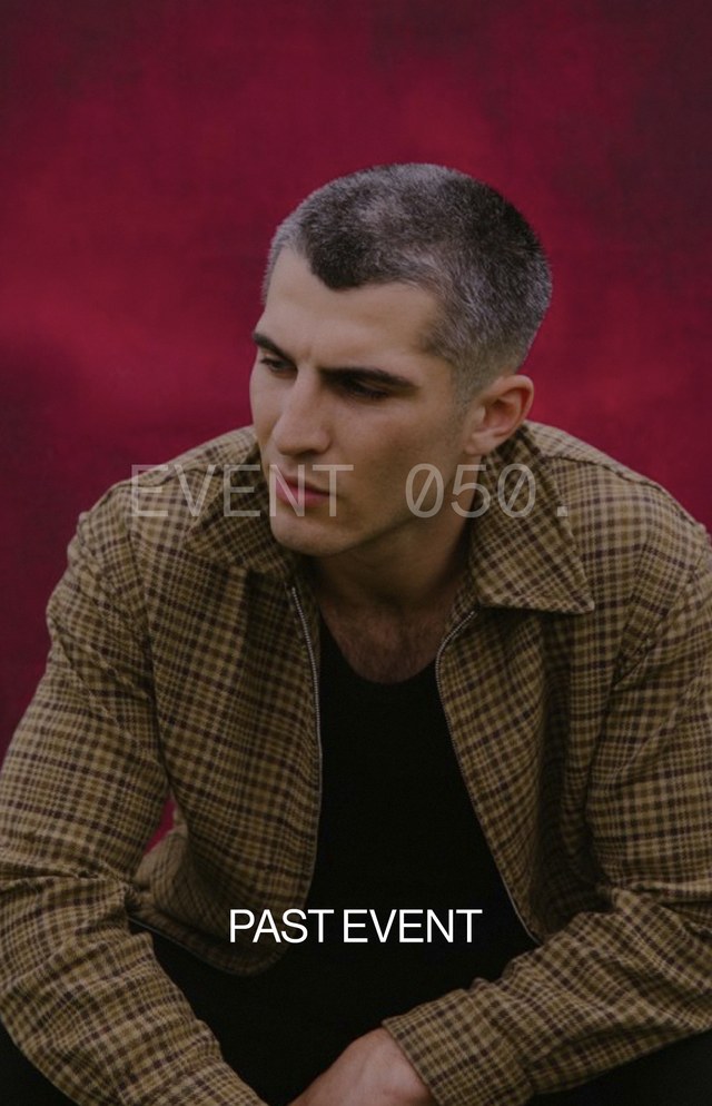 A man with short hair wearing a checkered shirt sits pensively against a deep red background. Text reads "EVENT 050." and "PAST EVENT."