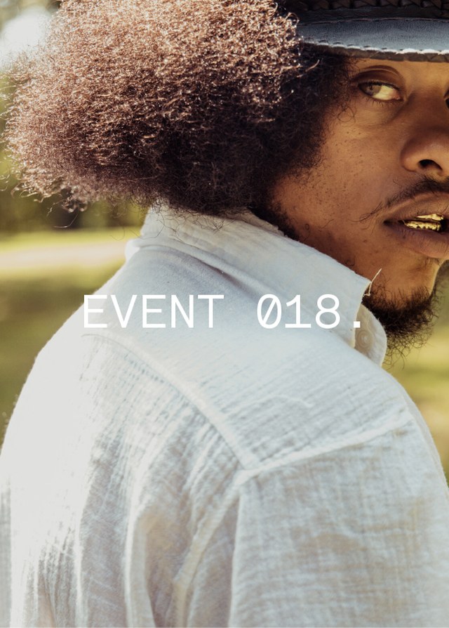 Person with afro hairstyle and a hat gazes at camera; wearing a white shirt. Text reads "EVENT 018."