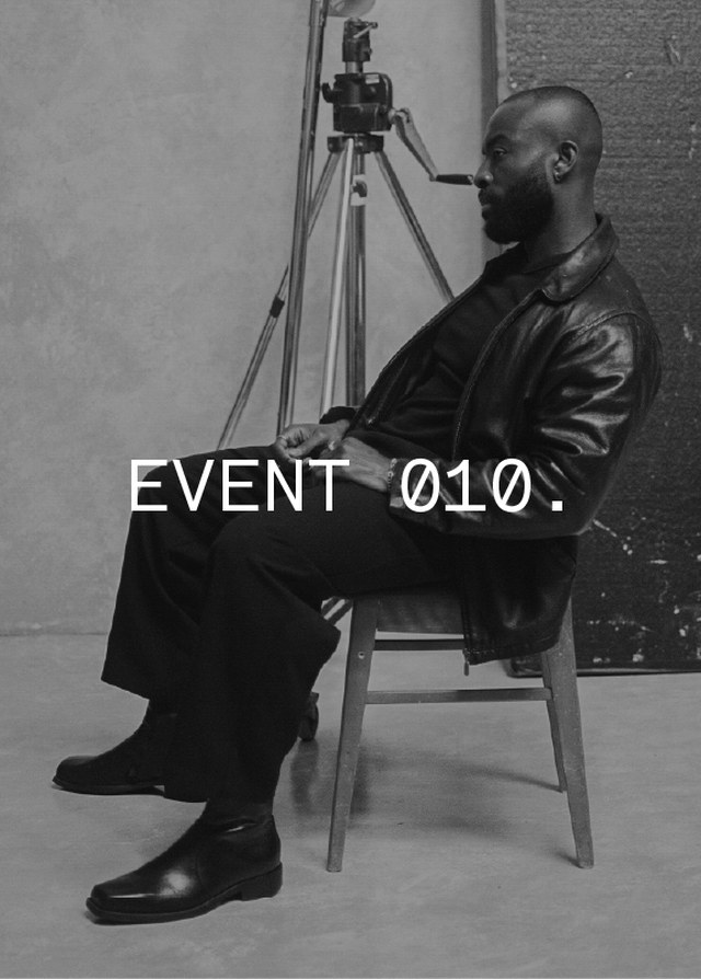 Man in a leather jacket sits on a chair in a studio setting with a tripod in the background; text reads "EVENT 010."