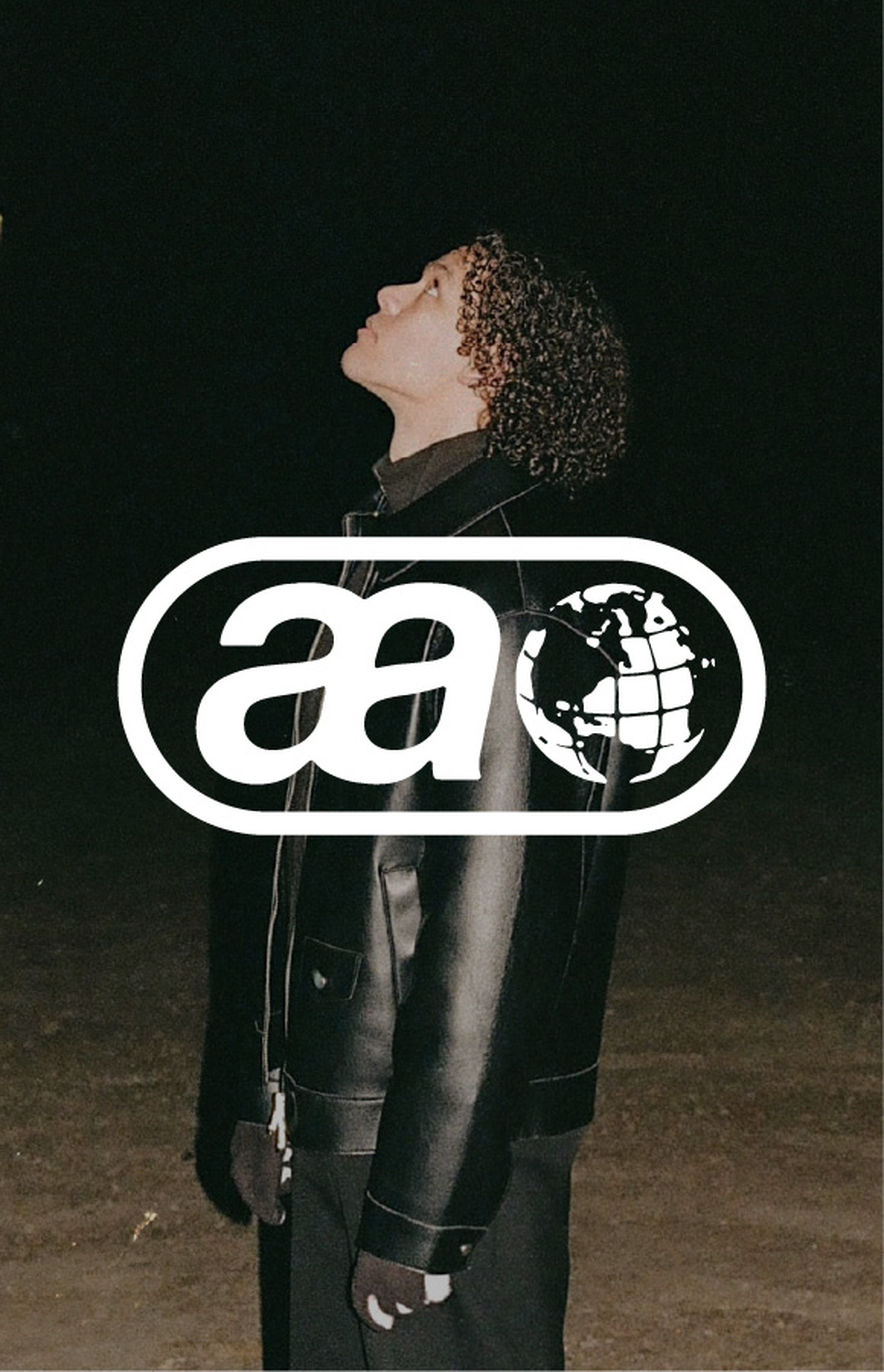 Person with curly hair in a leather jacket looks up at night. Logo of "aa" and a globe overlay the image.
