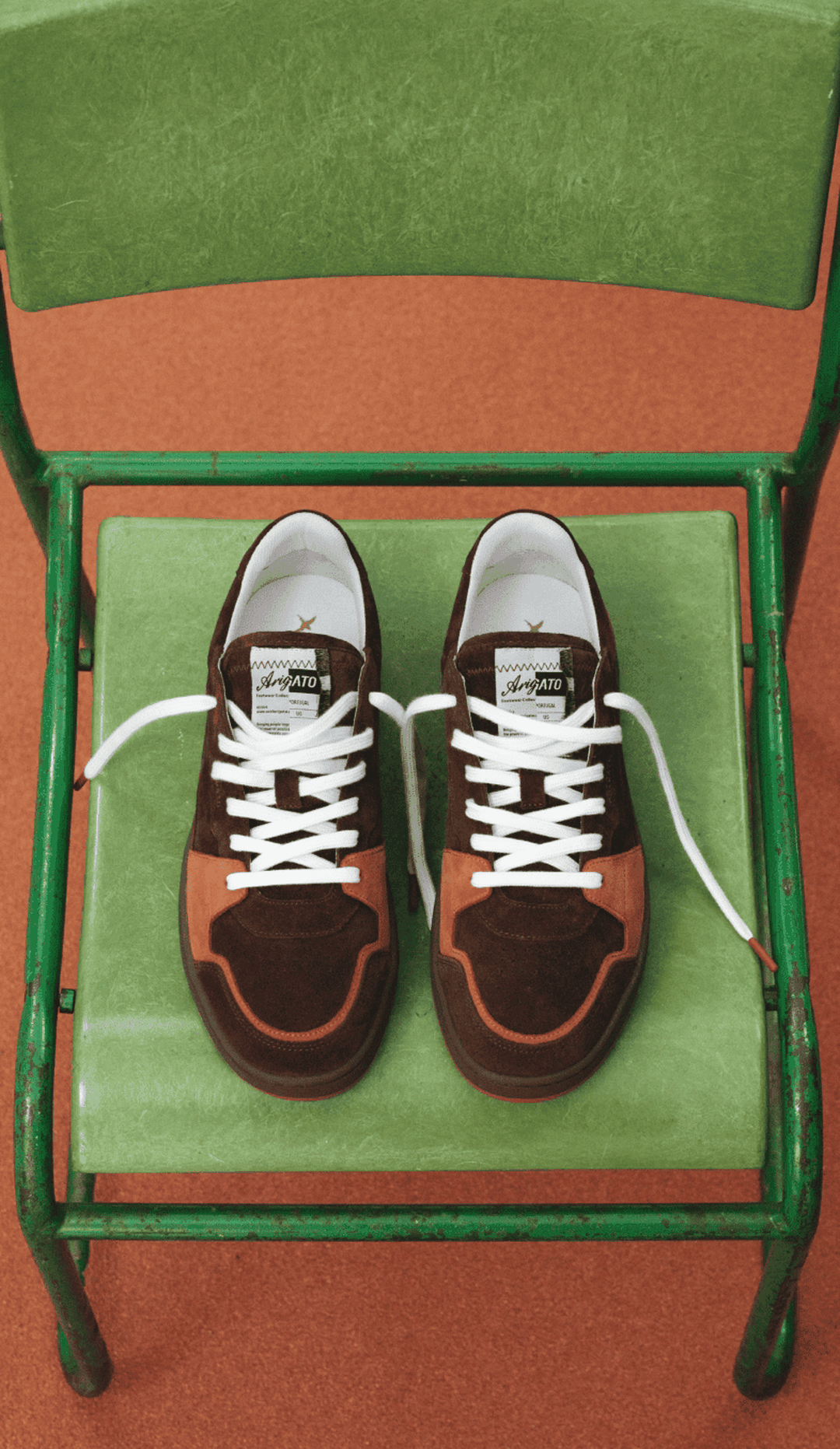 Brown and rust sneakers with white laces on a green chair with an orange floor background.