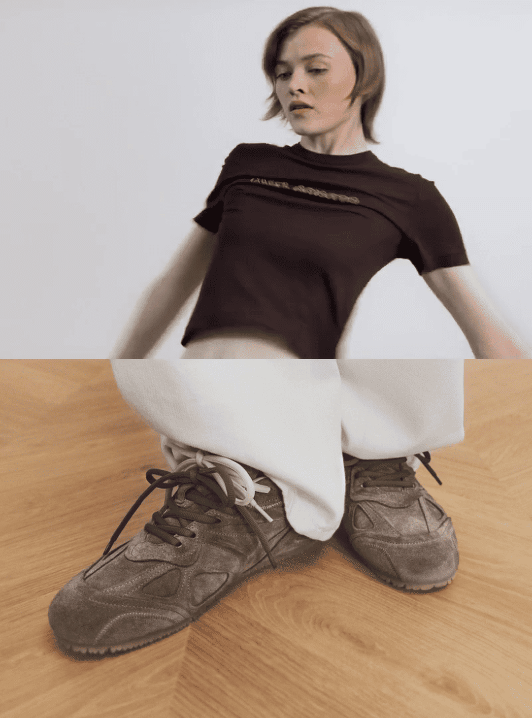 A person in a black shirt and white pants leans back; the lower half shows gray sneakers on a wooden floor.