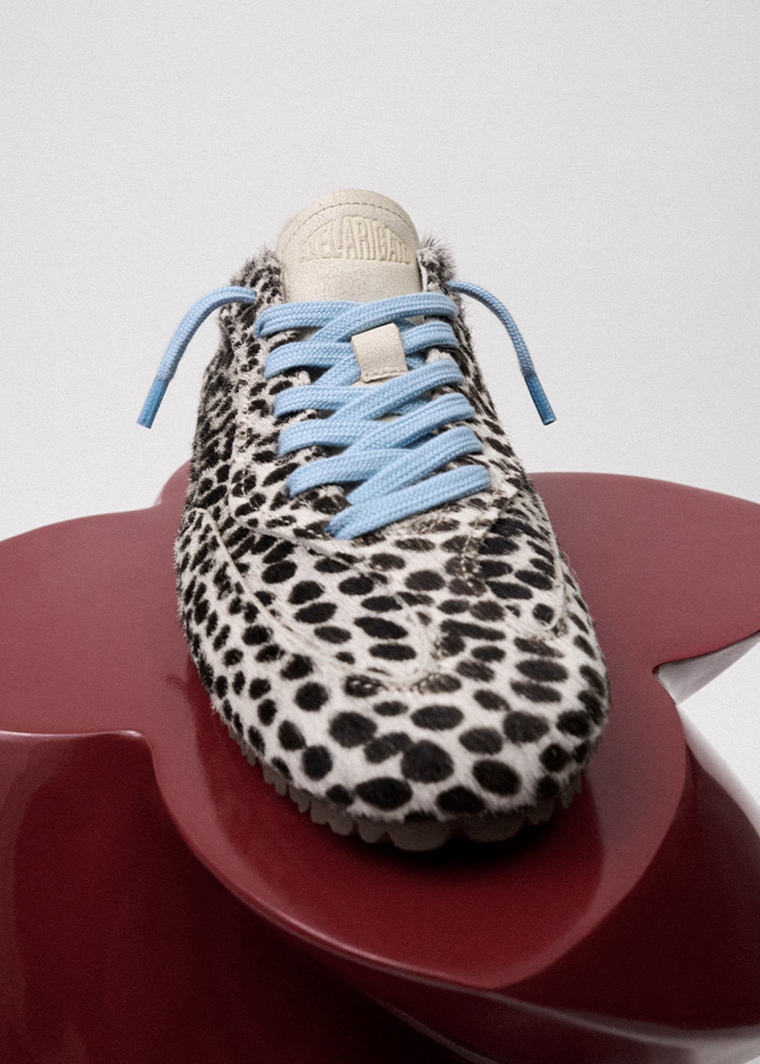 A leopard-print sneaker with blue laces displayed on a glossy red surface.