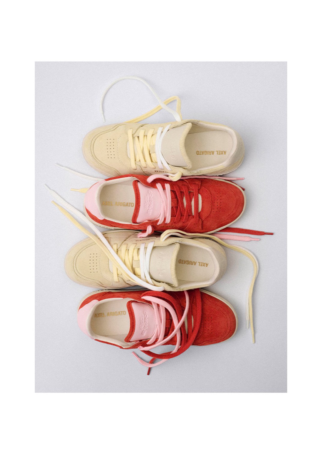 Four sneakers stacked in pairs, two beige and two red, with colorful laces tangled, on a light background.