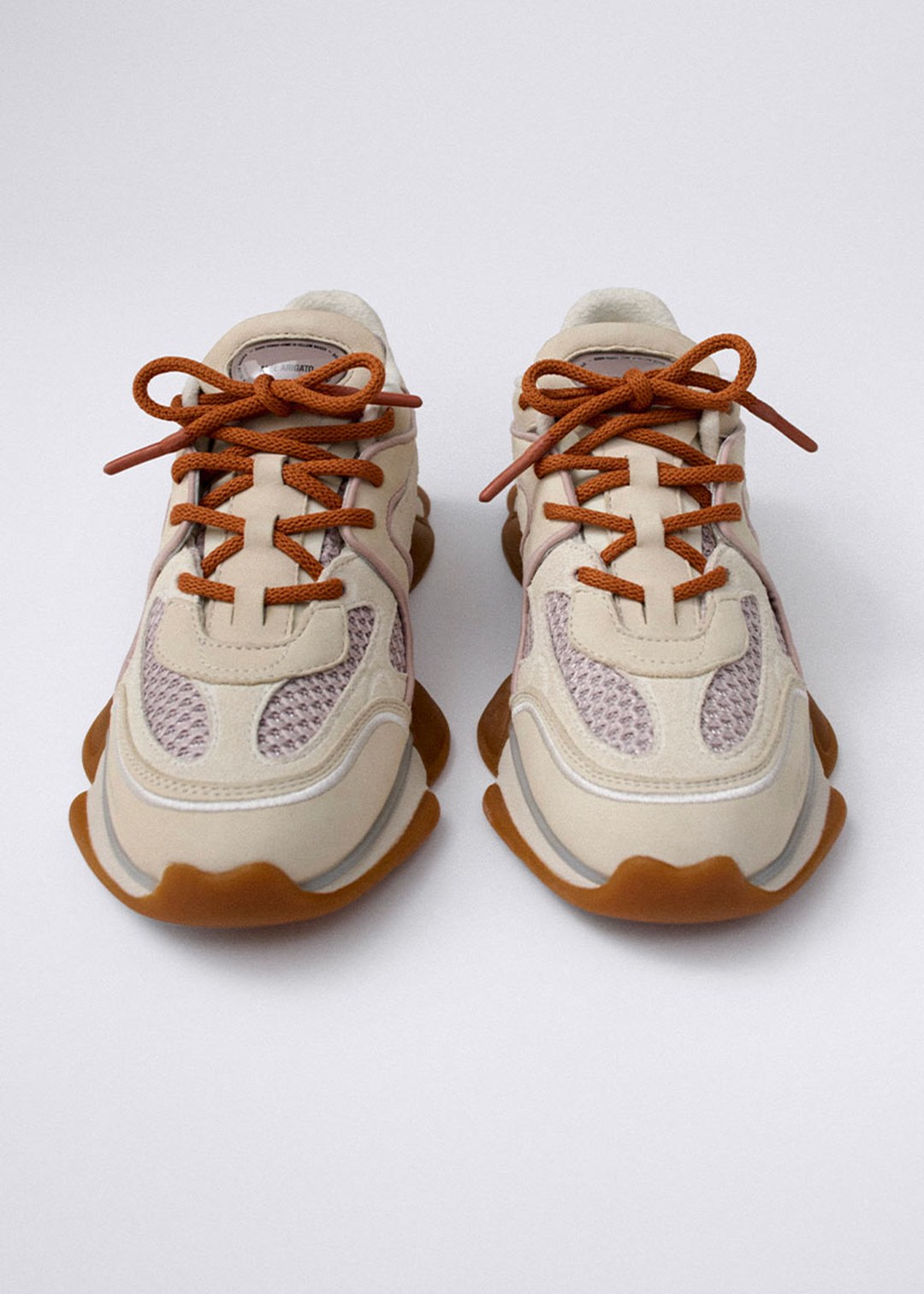 A pair of beige sneakers with brown laces and thick, wavy brown soles. The sneakers feature mesh panels for breathability.