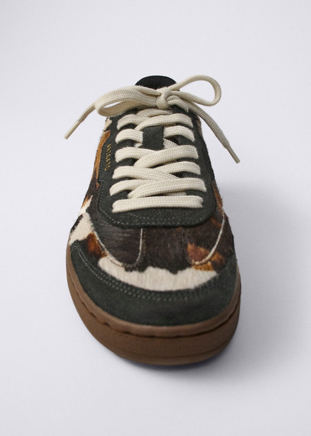 A stylish sneaker with a brown and white pattern, cream laces, and a brown sole, viewed from the front against a plain background.