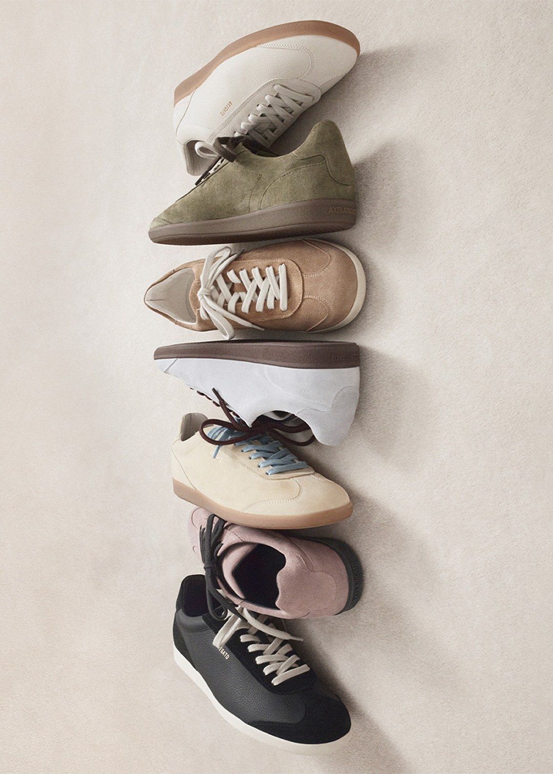 A vertical stack of six stylish sneakers in varying colors, including white, green, brown, blue, and black, arranged on a light background.