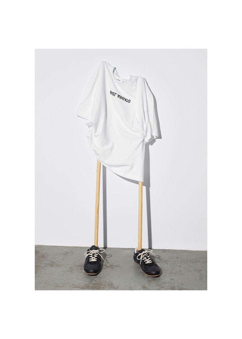 White T-shirt with "YES! VIVAYOU" text, draped over wooden sticks resembling legs, with black shoes on a concrete floor.