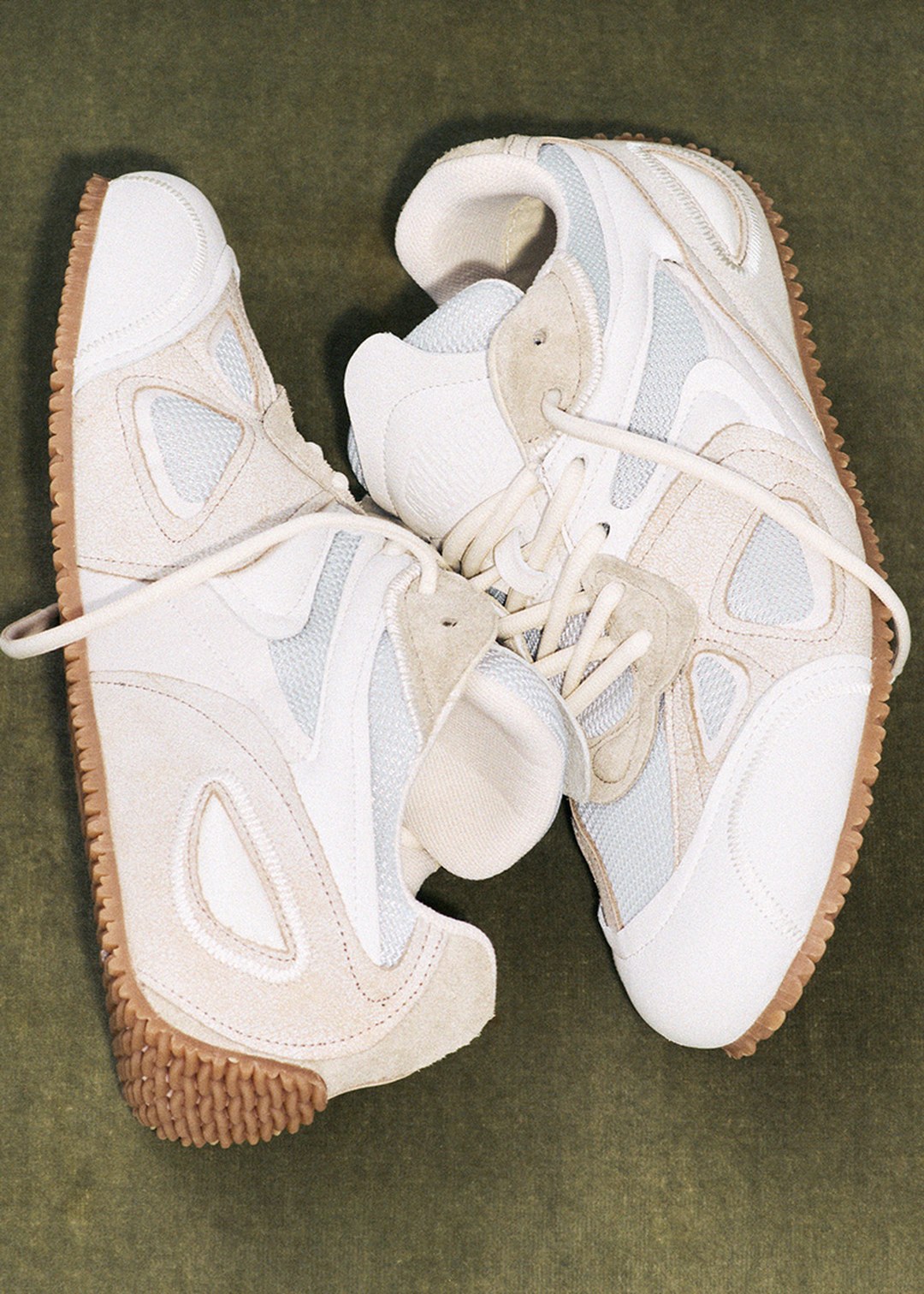 Two stylish sneakers with white and beige suede panels, white laces, and textured gum soles, placed on a green background.