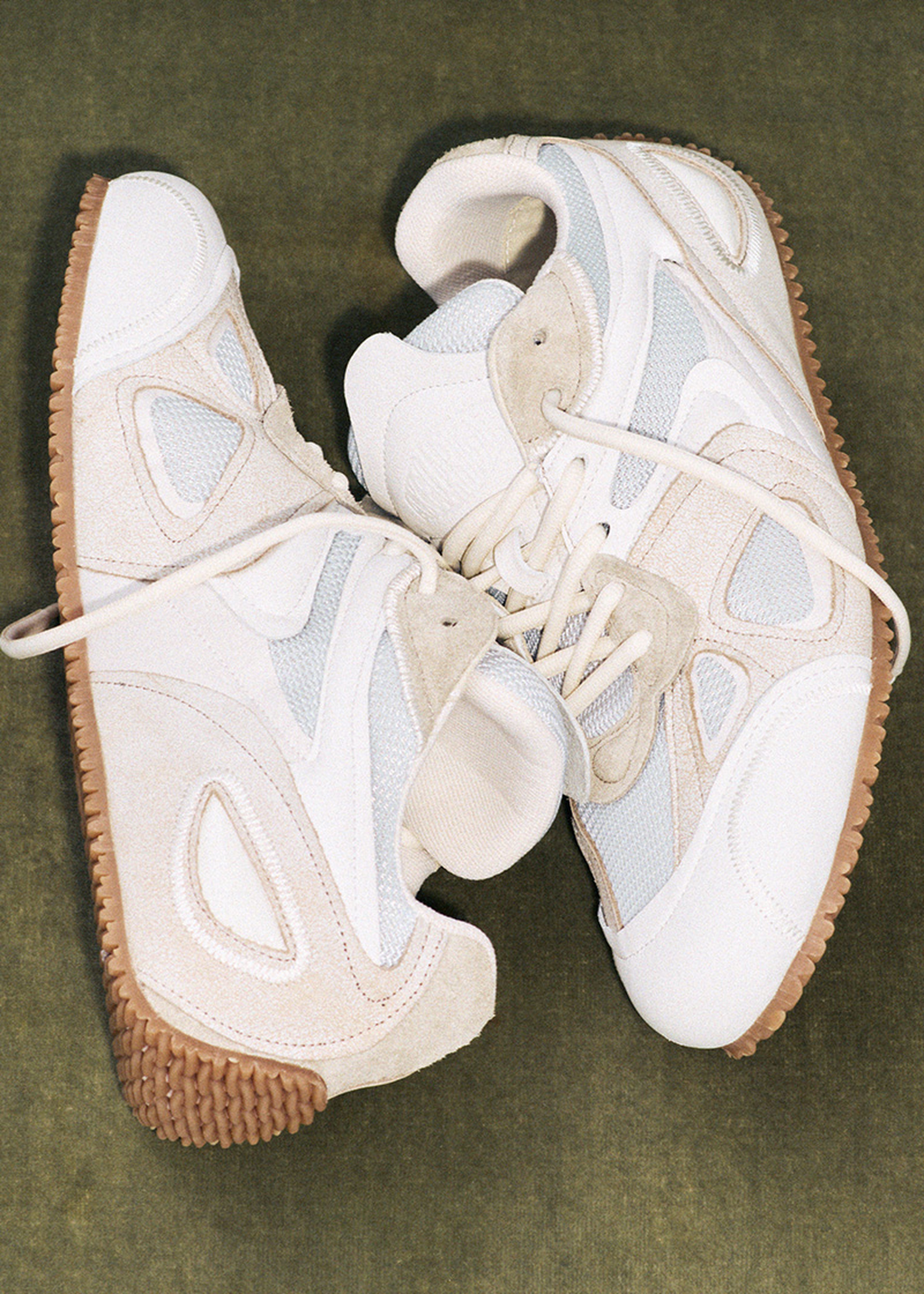 Two stylish sneakers with white and beige suede panels, white laces, and textured gum soles, placed on a green background.