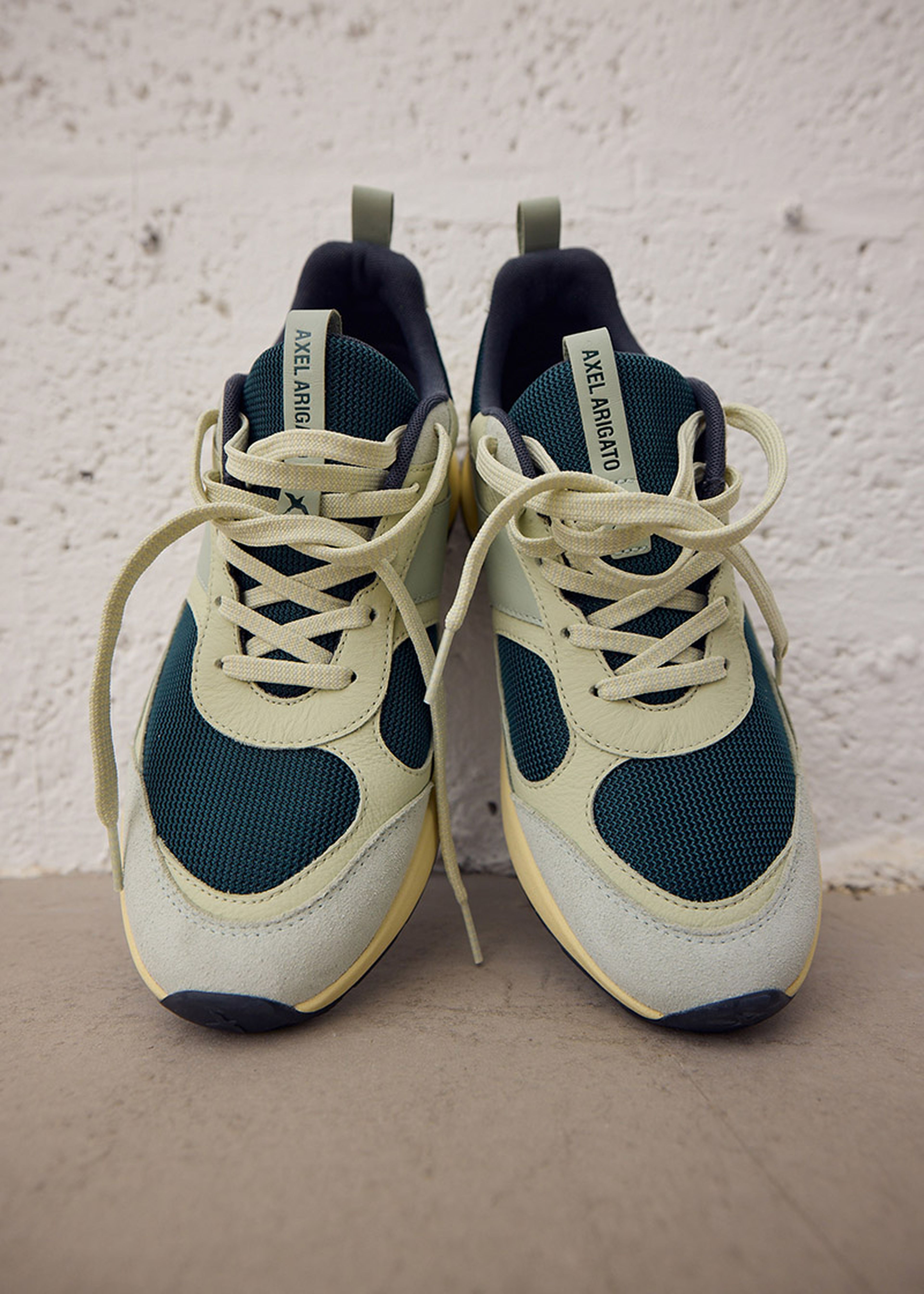 Pair of stylish sneakers with blue and cream panels, laced up and placed against a textured white wall.