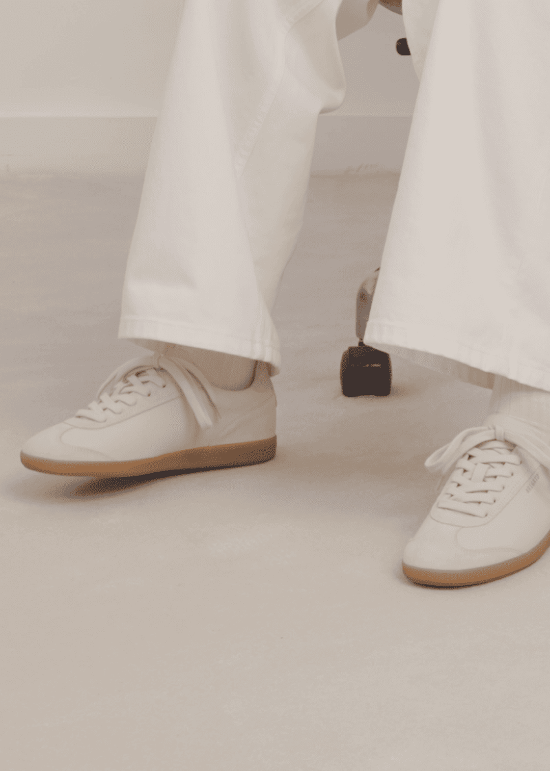 Person wearing white sneakers and wide-legged white pants, sitting on a chair. Sneakers have light brown soles.