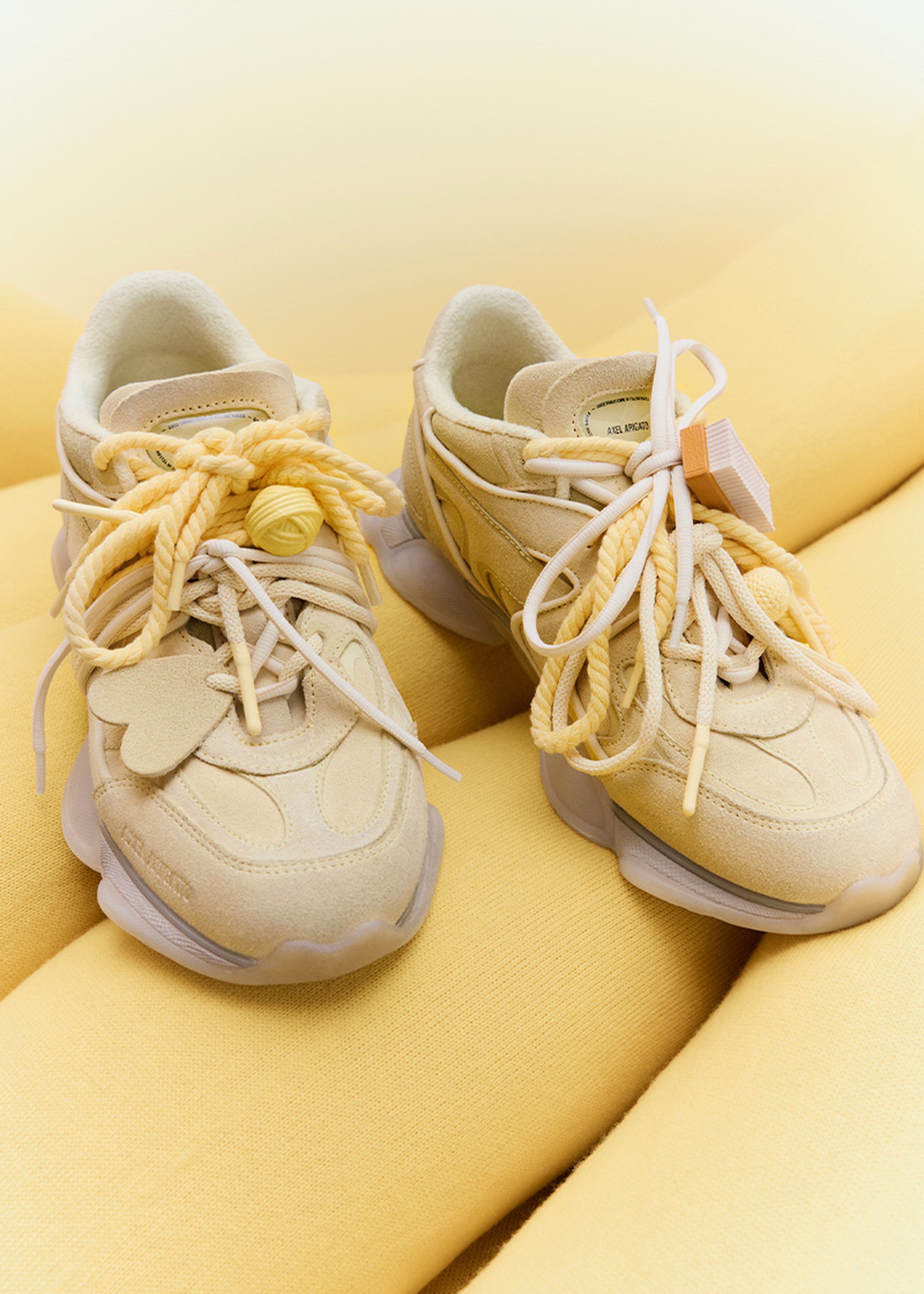 Yellow Eris sneakers with chunky soles and oversized yellow laces, displayed on a soft, yellow fabric background.