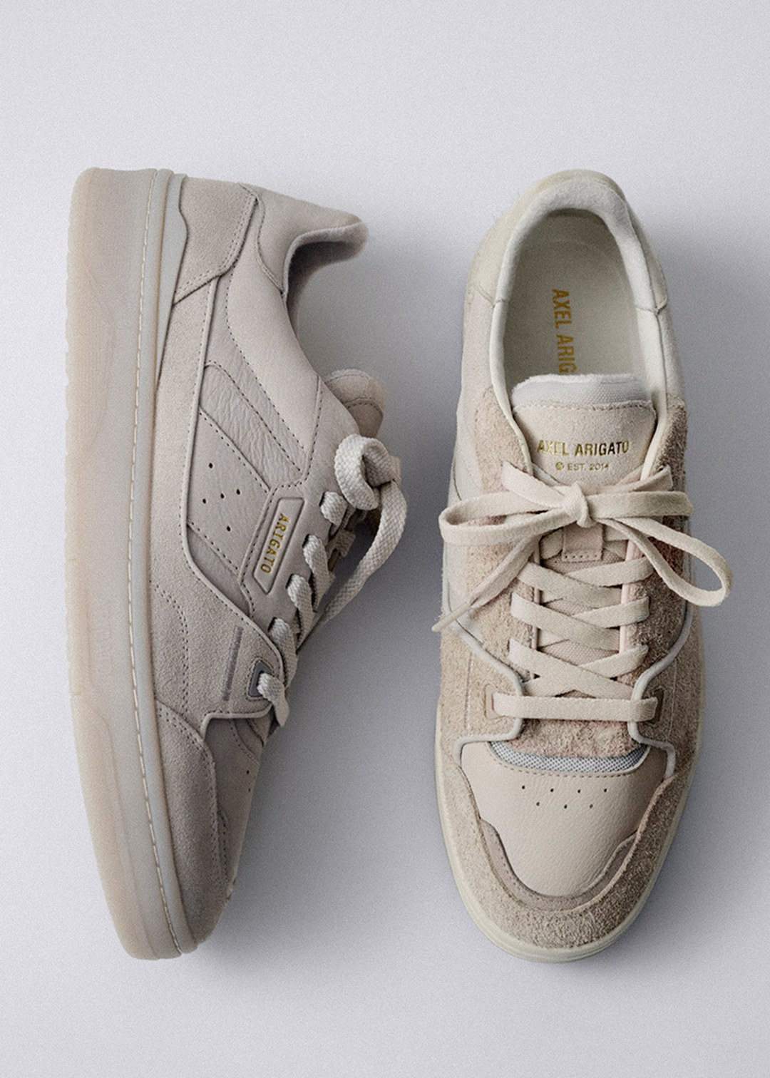 A pair of beige sneakers with suede details, one side view and one top view, on a light gray background.