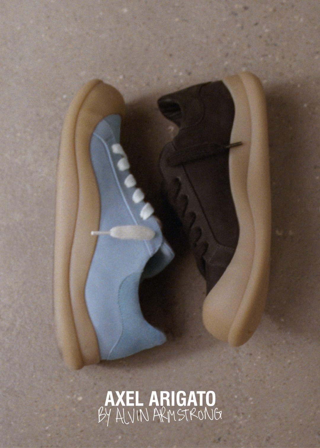 Two sneakers, one light blue and one dark brown, with gum soles, placed side by side on a textured surface. Text: "Axel Arigato by Alvin Armstrong."