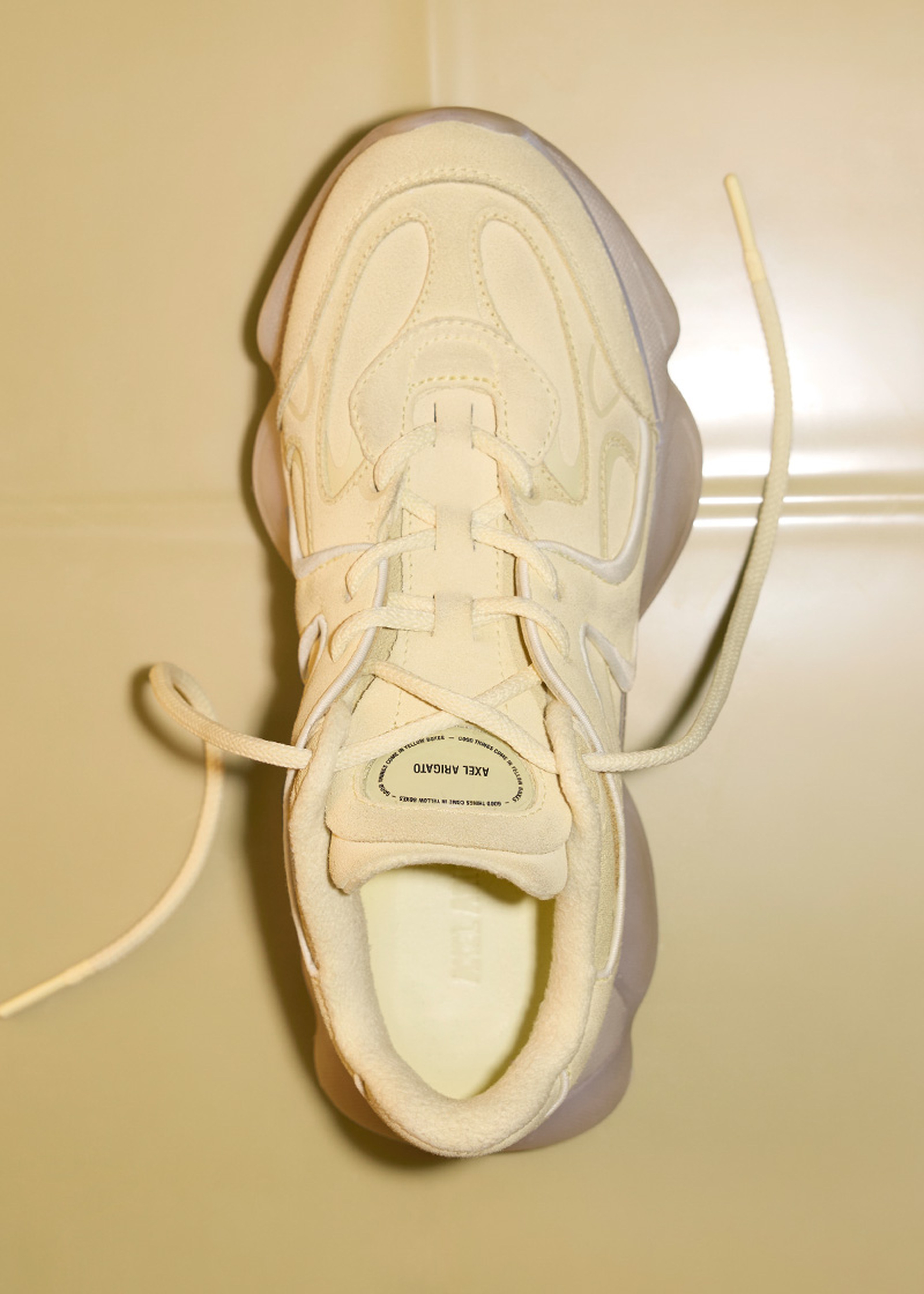 Top view of a cream-colored sneaker with textured patterns and visible laces, displayed on a light surface.