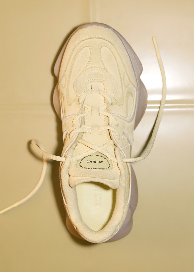 Top view of a cream-colored sneaker with textured patterns and visible laces, displayed on a light surface.