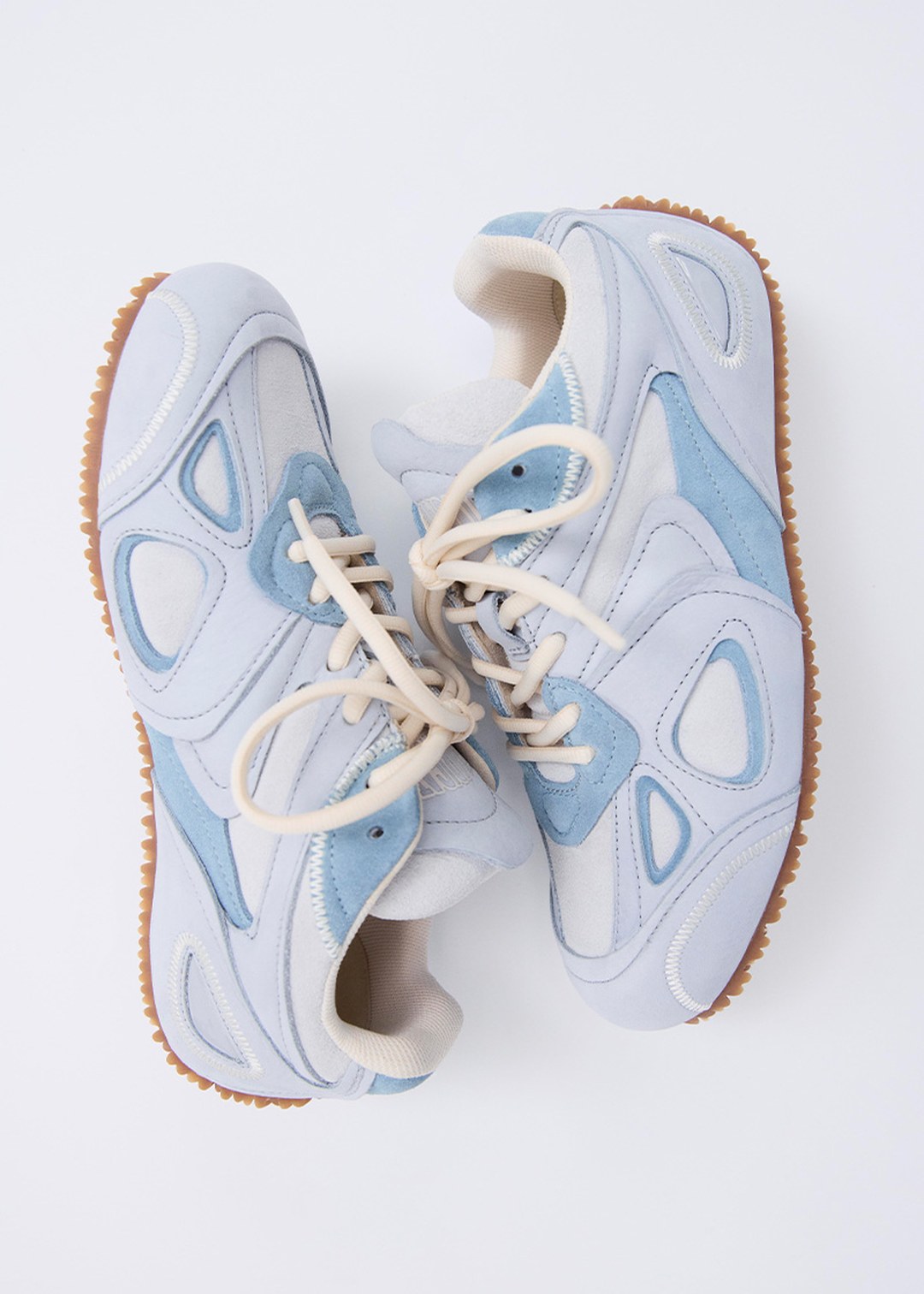 Pair of stylish light blue and white sneakers with beige laces and brown soles, arranged side by side on a white background.