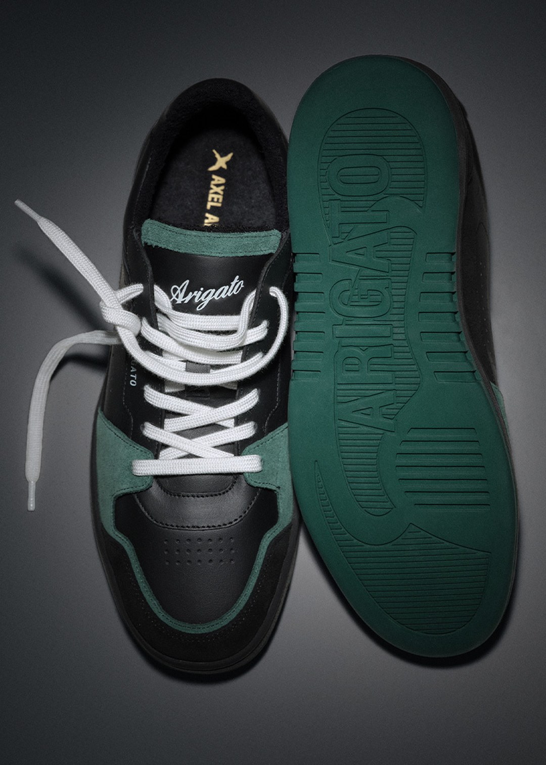 Black and green sneaker with white laces, next to an outsole with "Arigato" embossed, on a dark background.