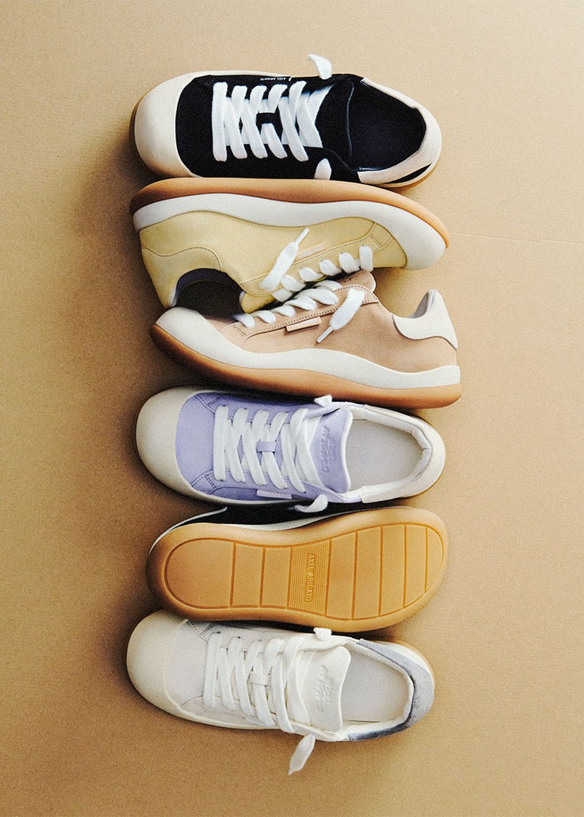 Five pairs of sneakers in various colors, stacked vertically on a beige background.