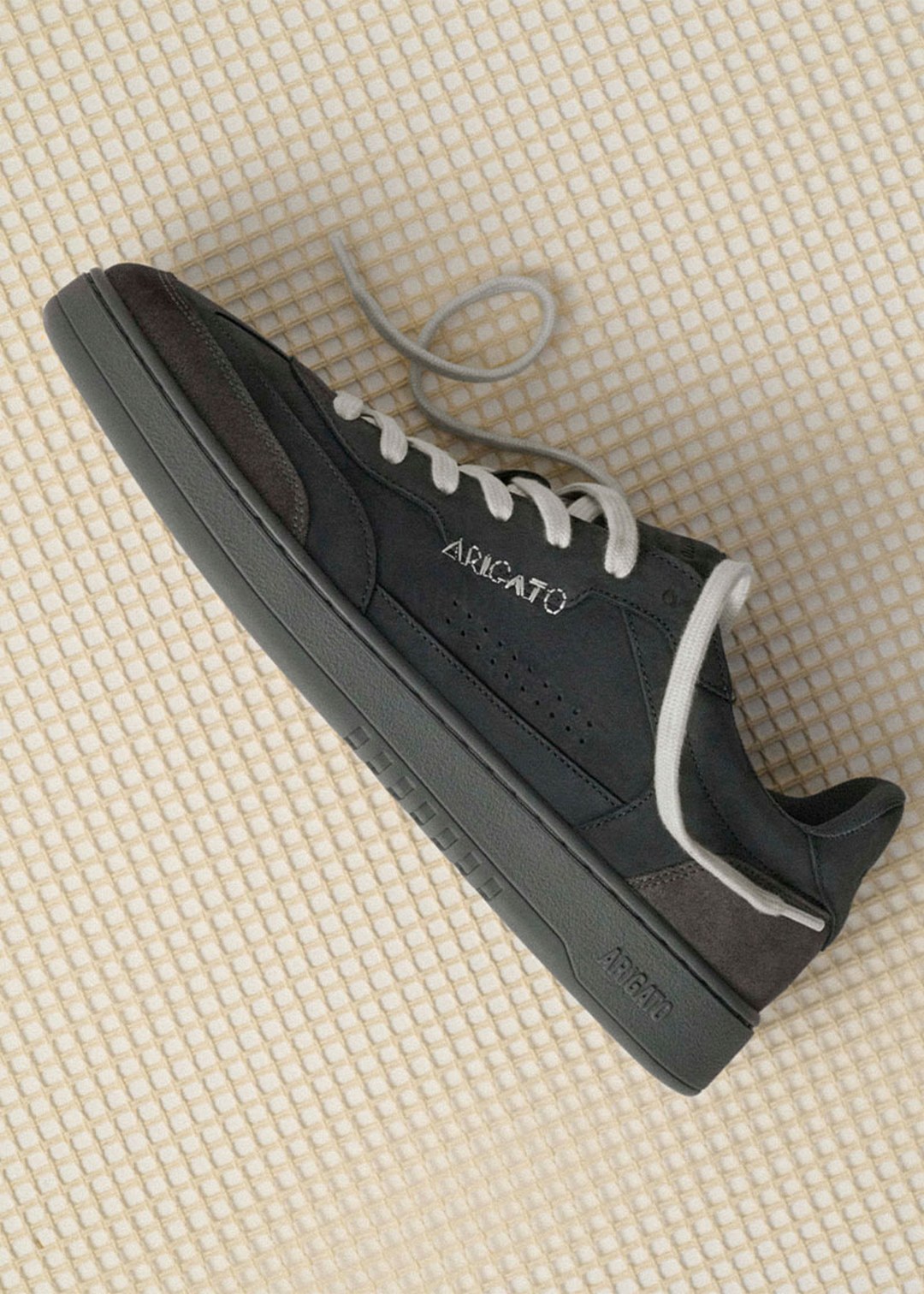 Black Arcato sneaker with white laces and gray sole, placed on a light-checkered surface.