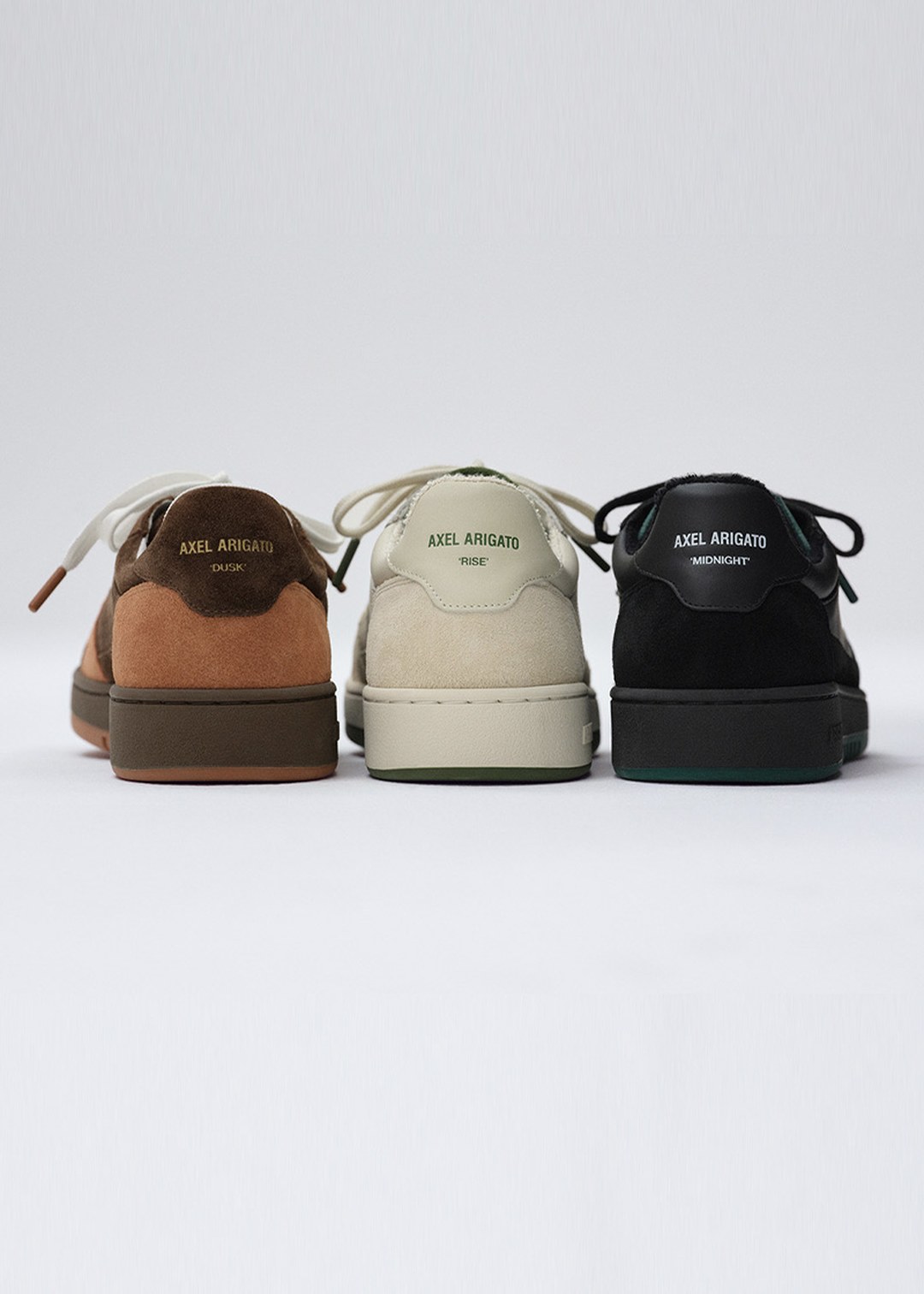 Three pairs of Axel Arigato sneakers in brown, beige, and black, viewed from the back against a plain background.