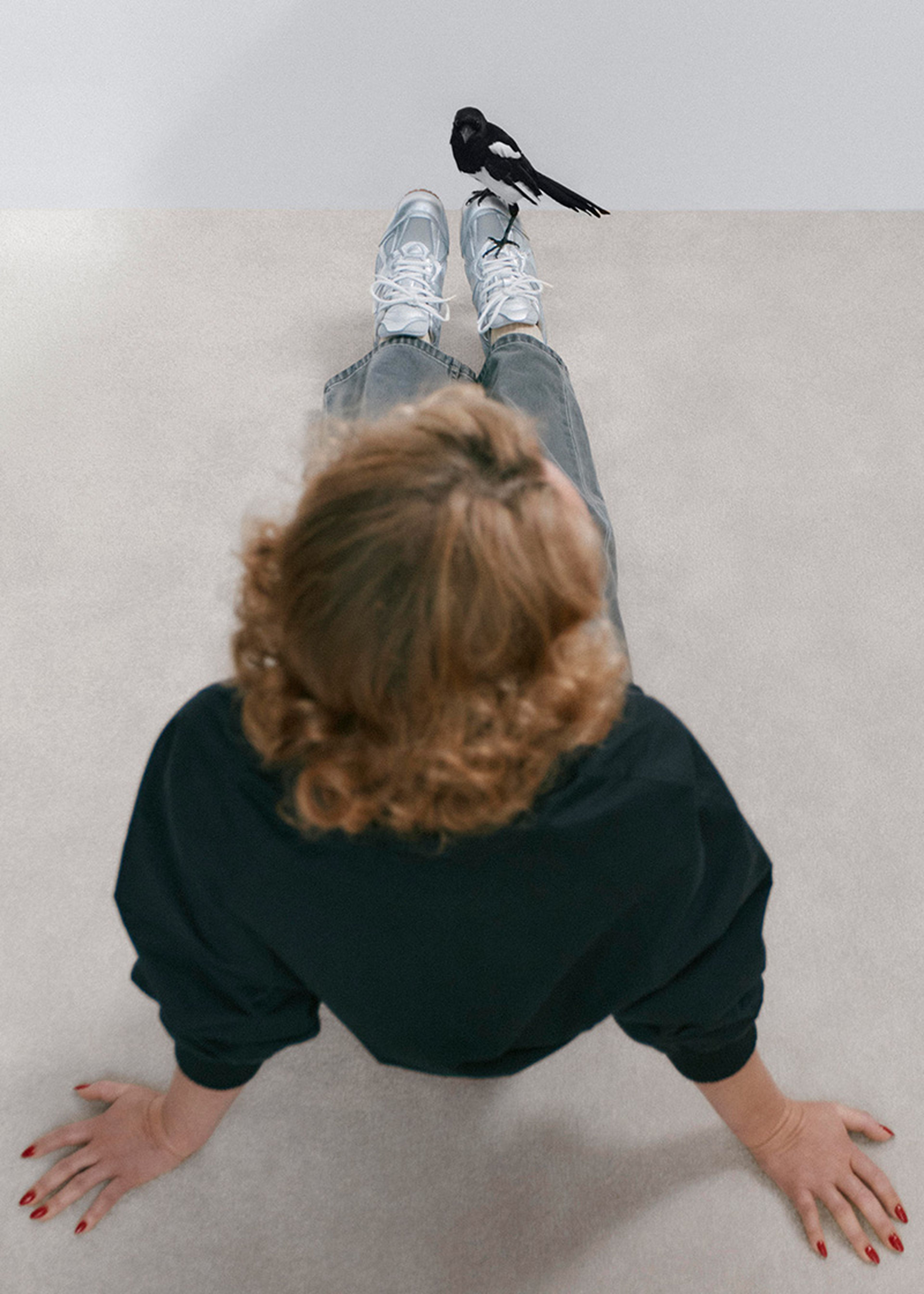 A person sitting on the floor with a bird perched on their shoelace, viewed from above.