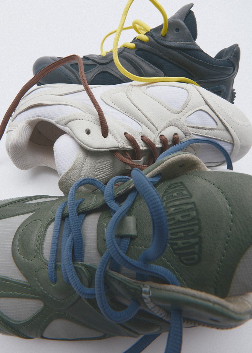 Three sneakers stacked with tangled laces in yellow, brown, and blue, featuring a mix of green, white, and dark gray colors.