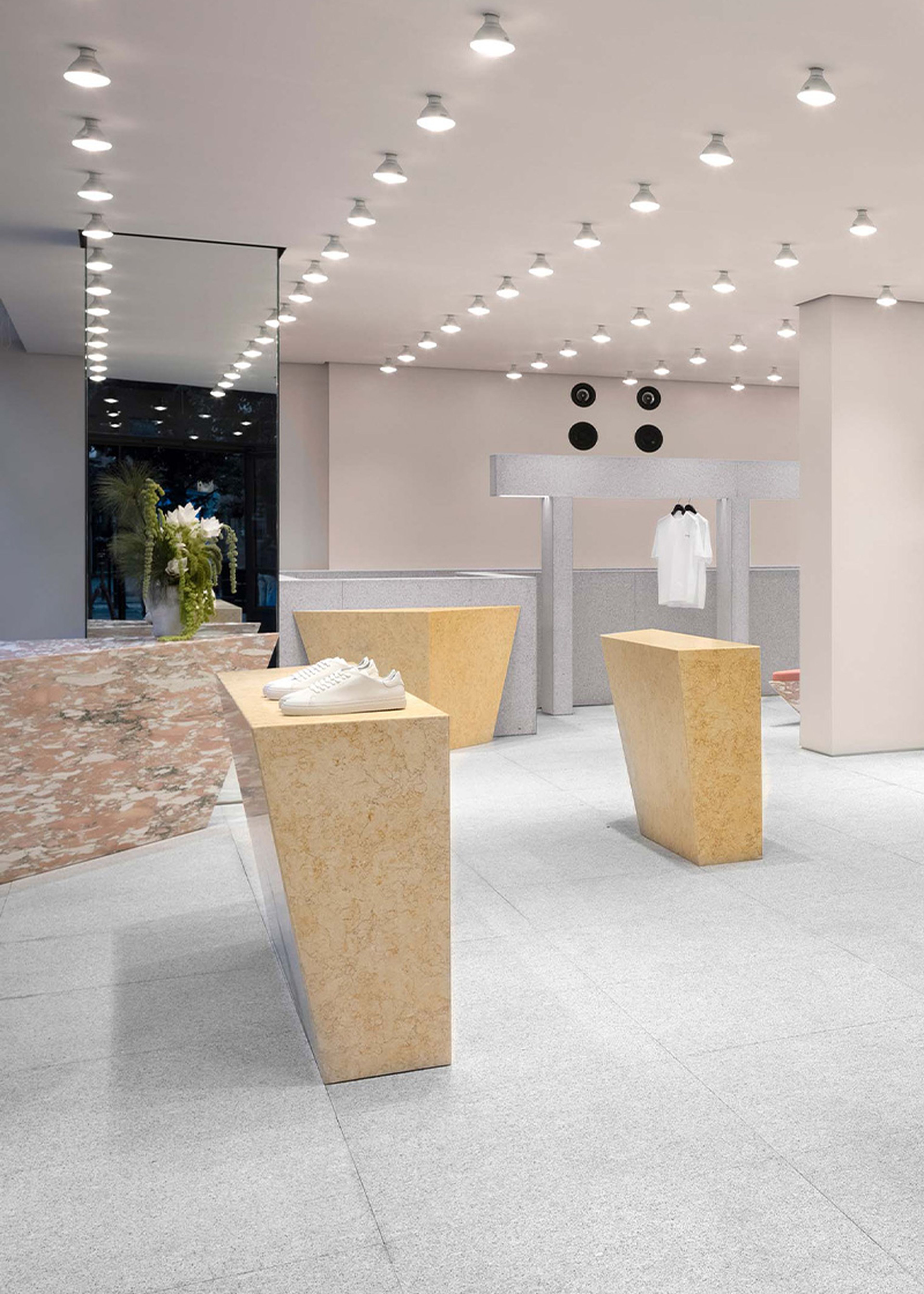 Modern retail store interior with minimalist design, featuring geometric display stands, overhead lighting, and a few clothing items on display.