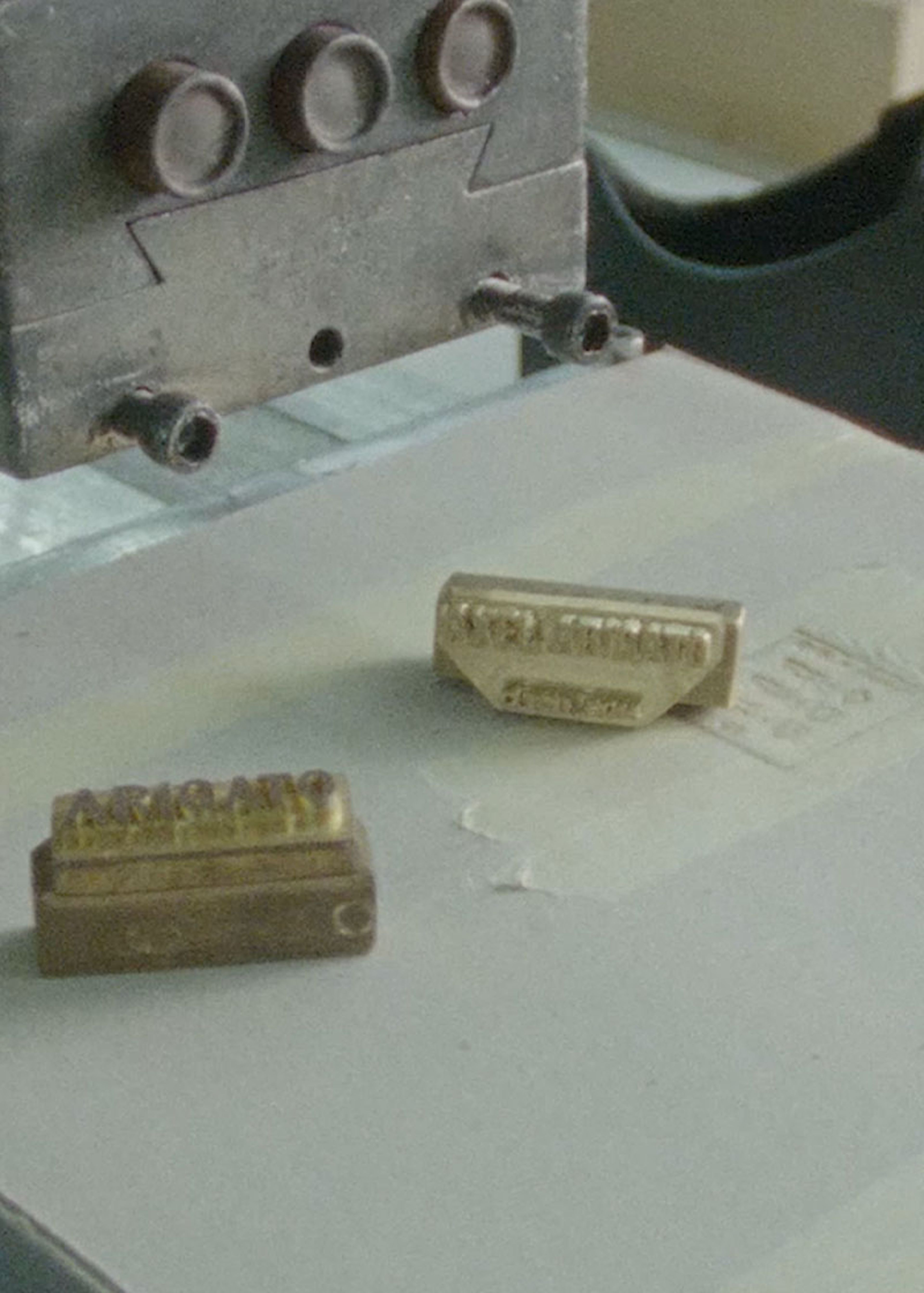 Close-up of a metal embossing machine with two brass stamps on a flat surface, one stamped with "PARIS FRANCE."