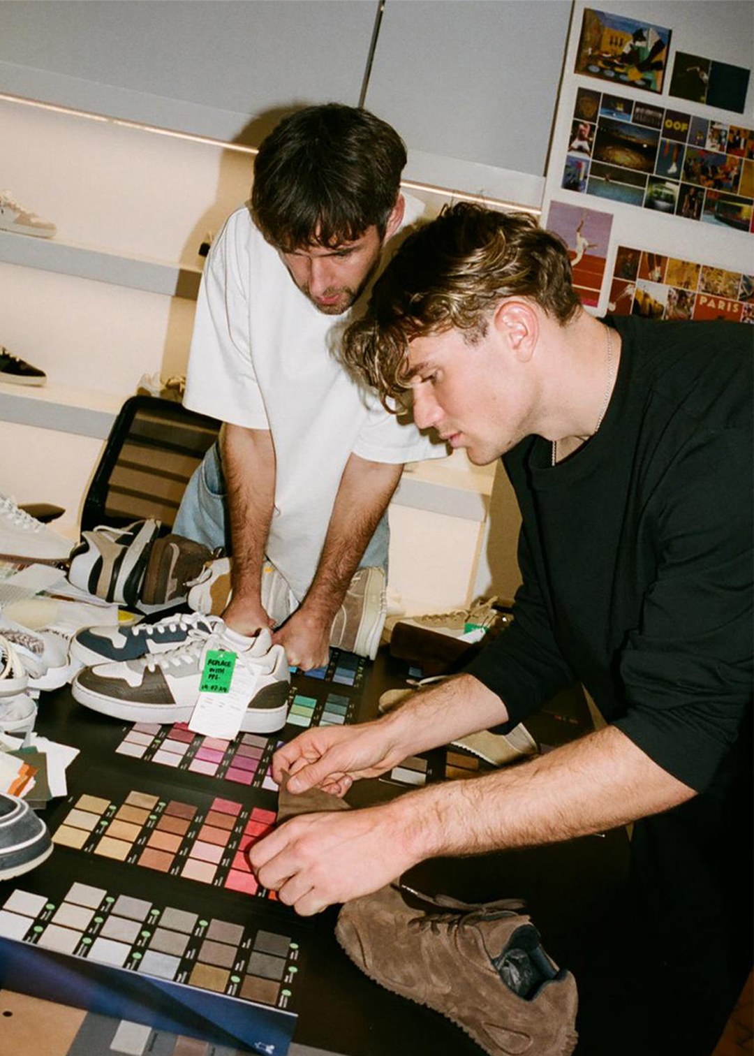 Two people examining color swatches and sneakers on a table, possibly working on shoe design or selection in a studio setting.