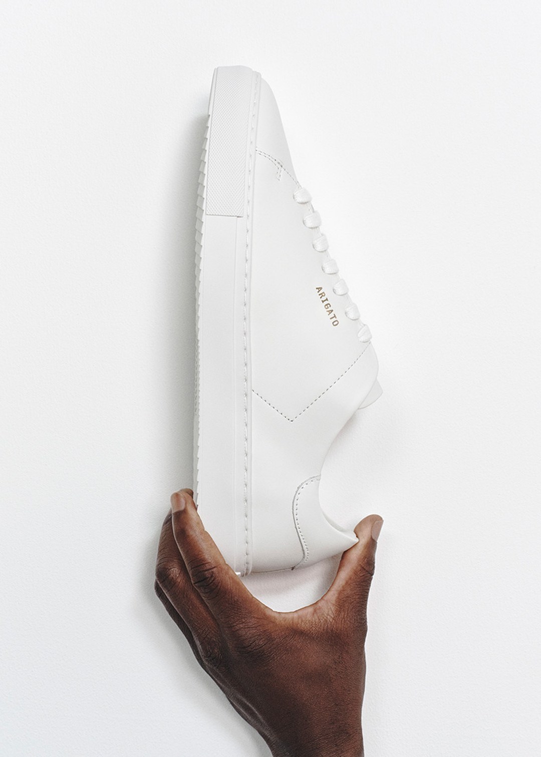 A hand holding a clean white sneaker with a minimalist design against a white background.