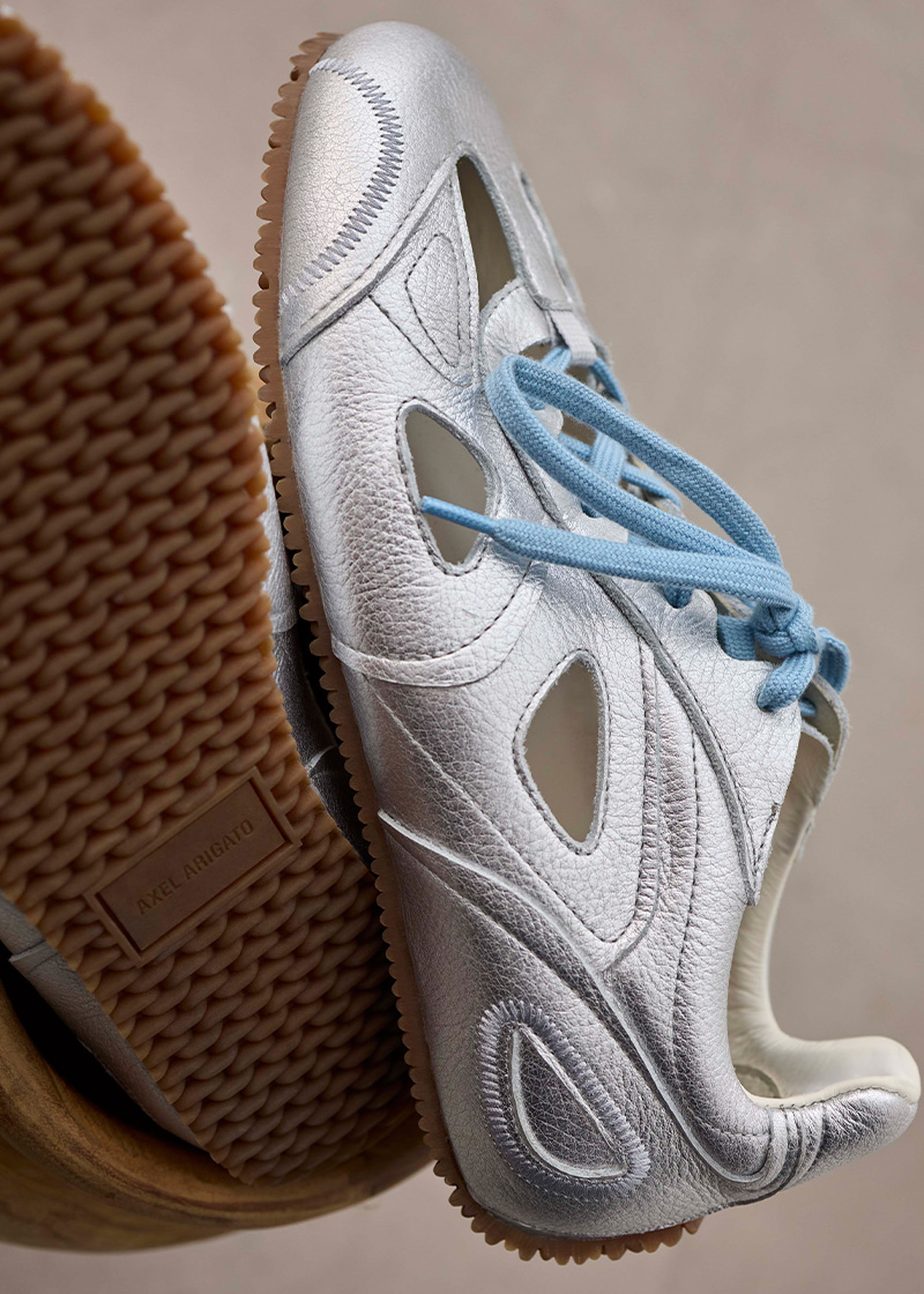 Silver leather sneaker with blue laces, featuring cut-out designs and a textured rubber sole.
