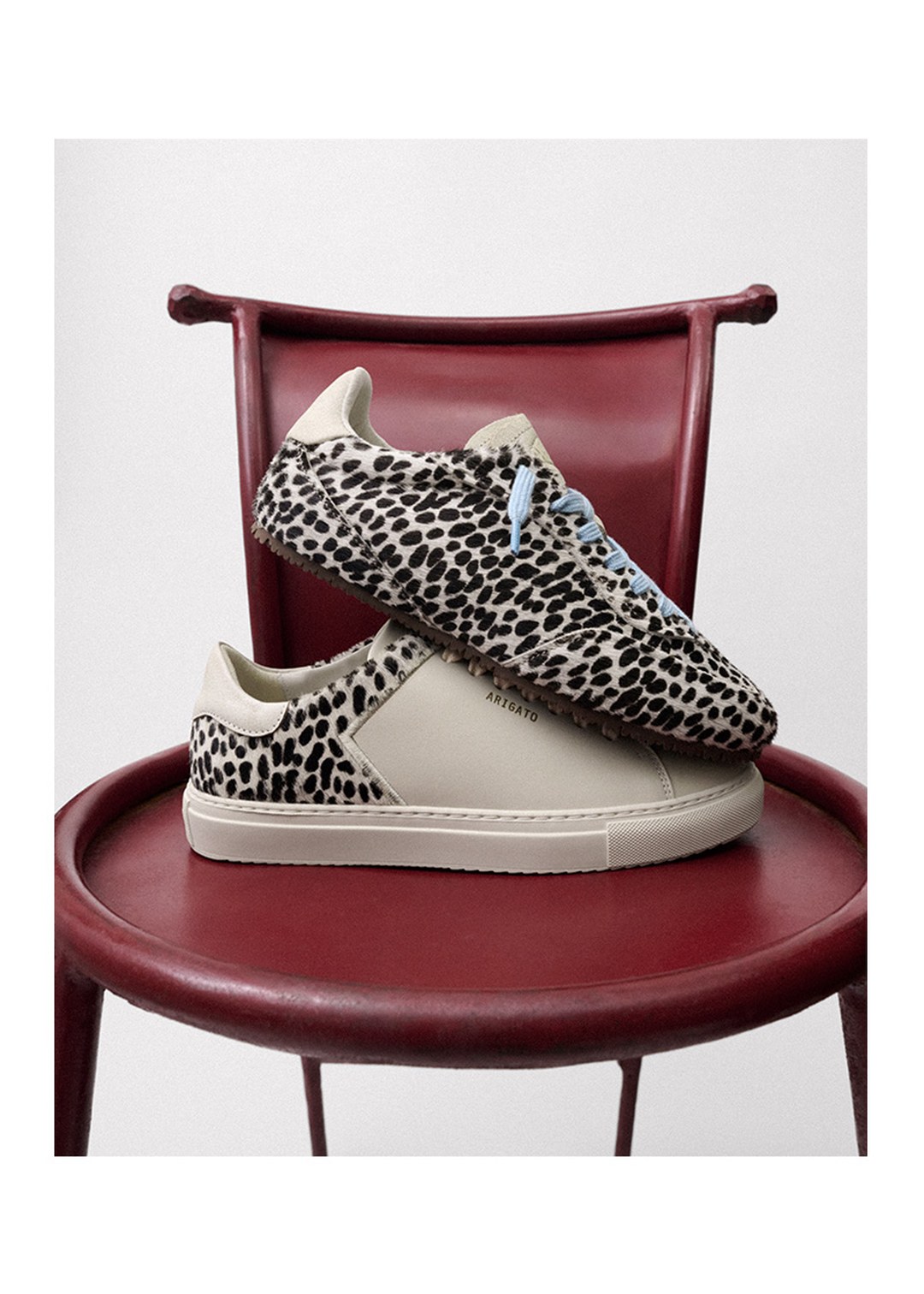 Leopard print sneakers with light blue laces are displayed on a red chair against a white background.